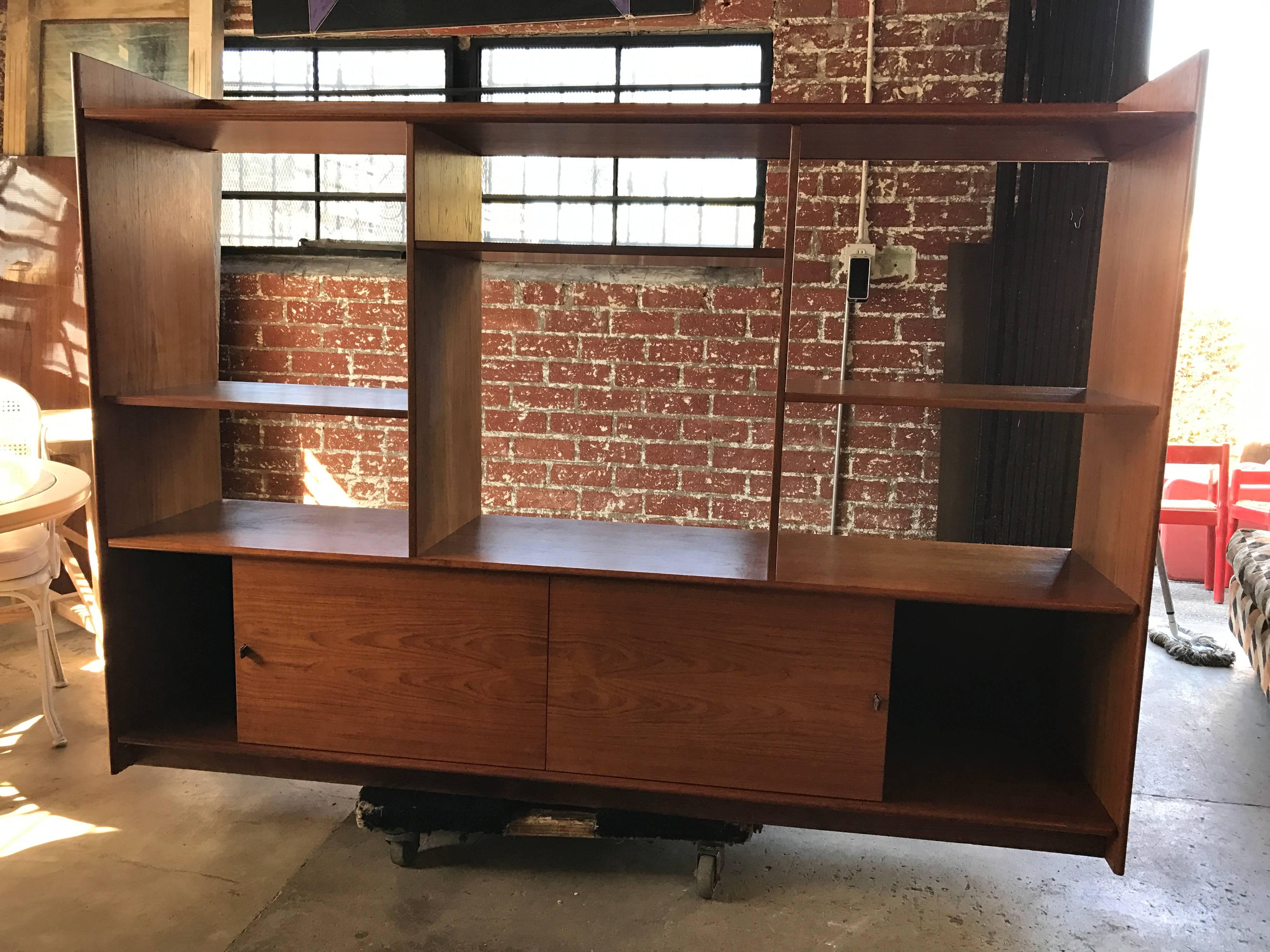 Teak Danish bookshelf features multiple sections and two sliding doors at bottom. There are brown leather pull on the sliding doors.
