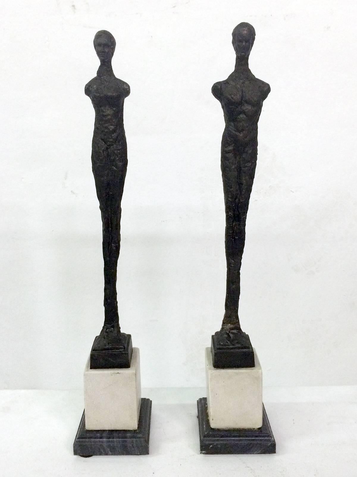Two figures, one a male and the other one a female on square stepped marble bases. The two stylized standing figures are made of cast resin after original clay sculptures.
