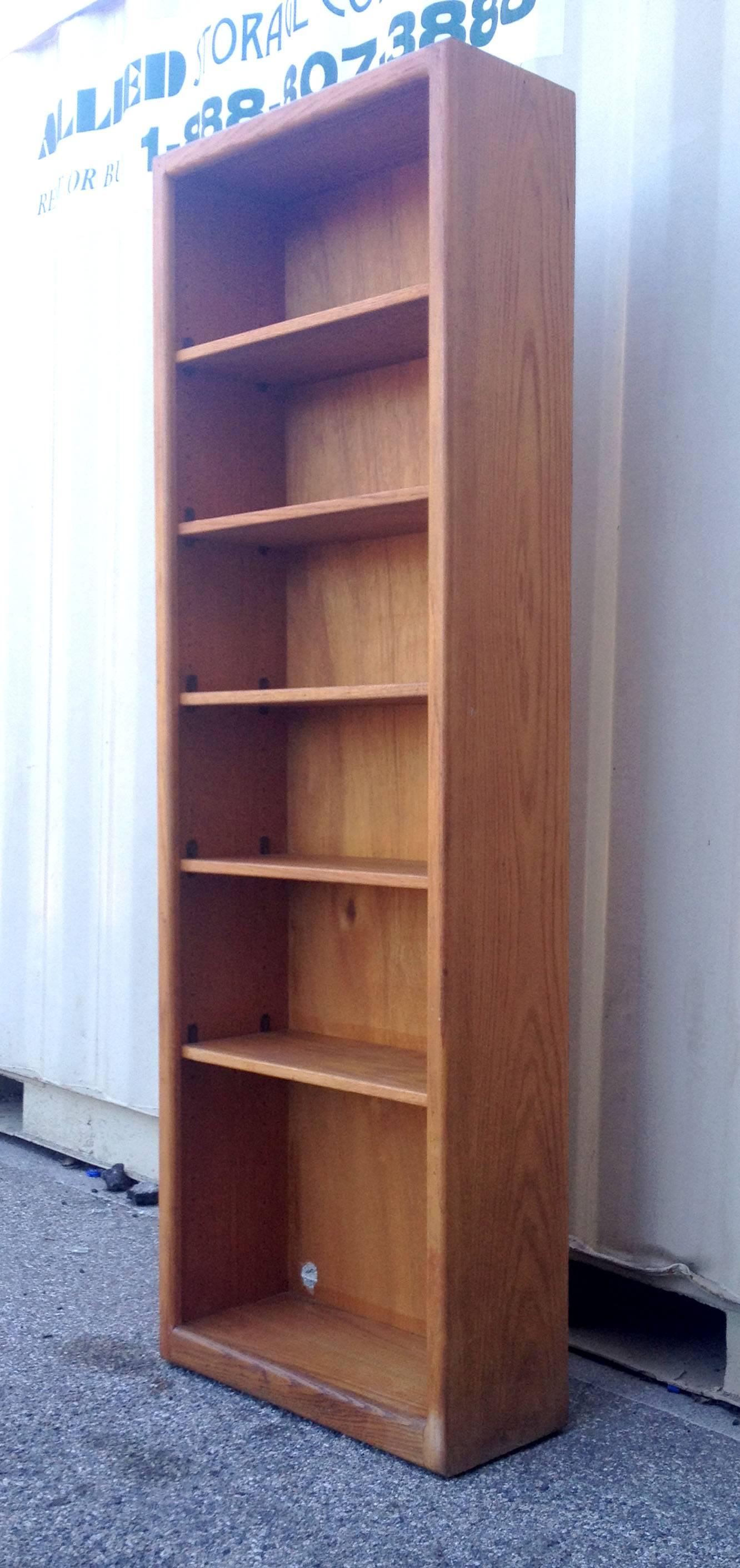 Tall an narrow teak bookshelf by Gerald McCabe that comes with five shelves which are adjustable. There is a small circle cut-out in the bottom of the piece in our photo which has been pierced by the original owner to let through electrical wiring.