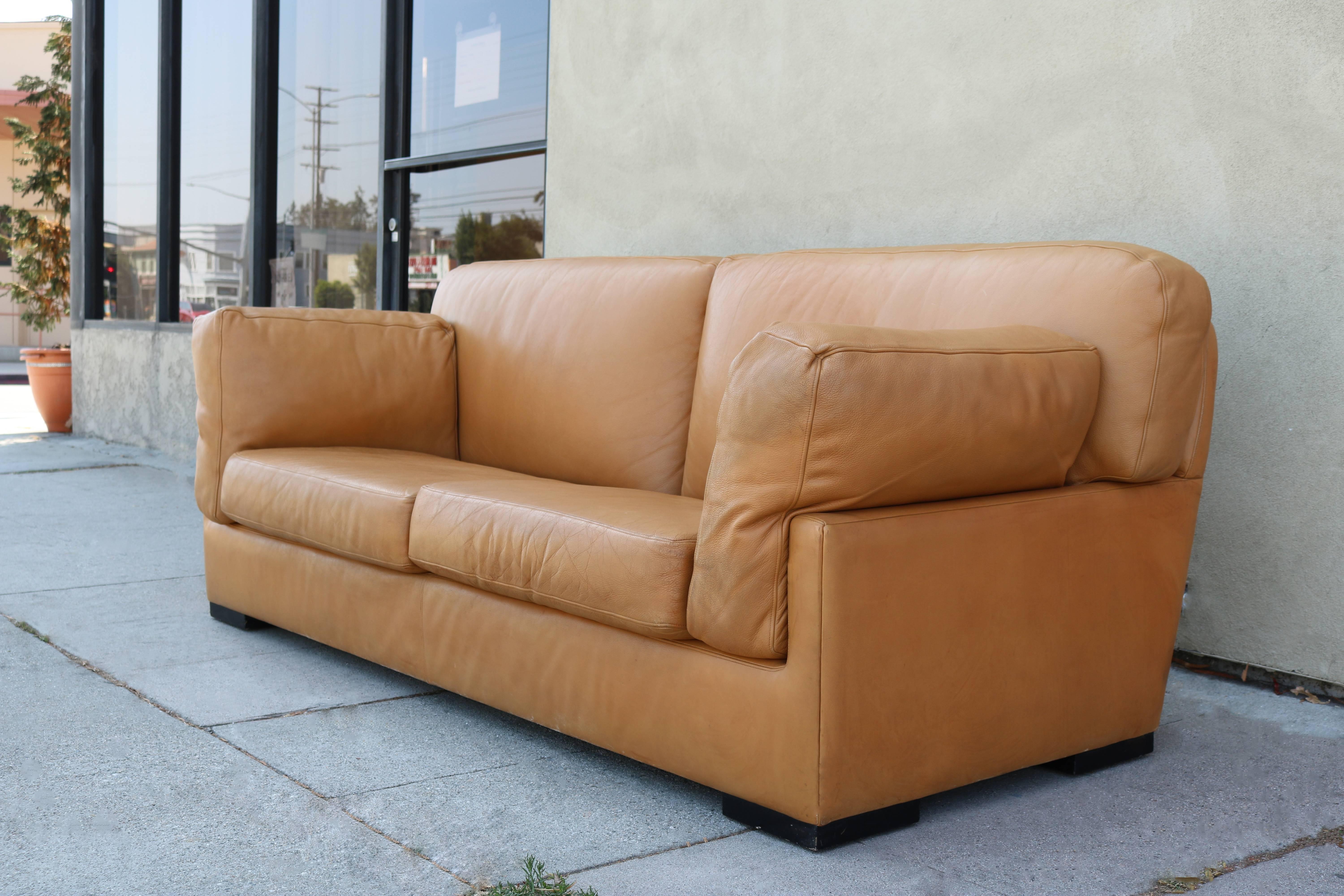 1970s era sofa covered in a warm, butterscotch colored thick and soft leather. It sits on four black square feet. Cushions have been newly re stuffed.