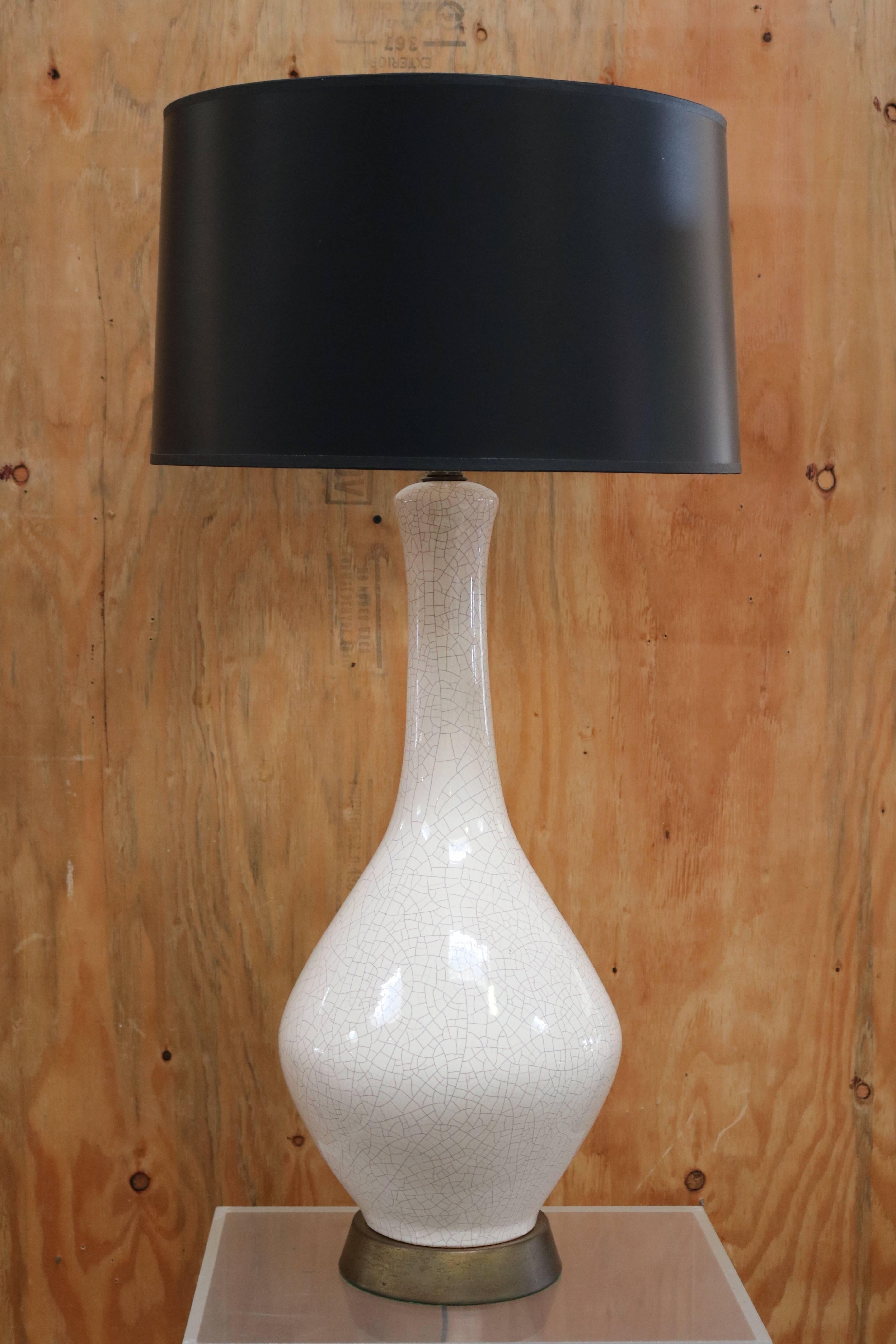 This table lamp has a vase-shaped body in white crackled ceramic. It sits on a round brass base and has a black paper custom-made shade.