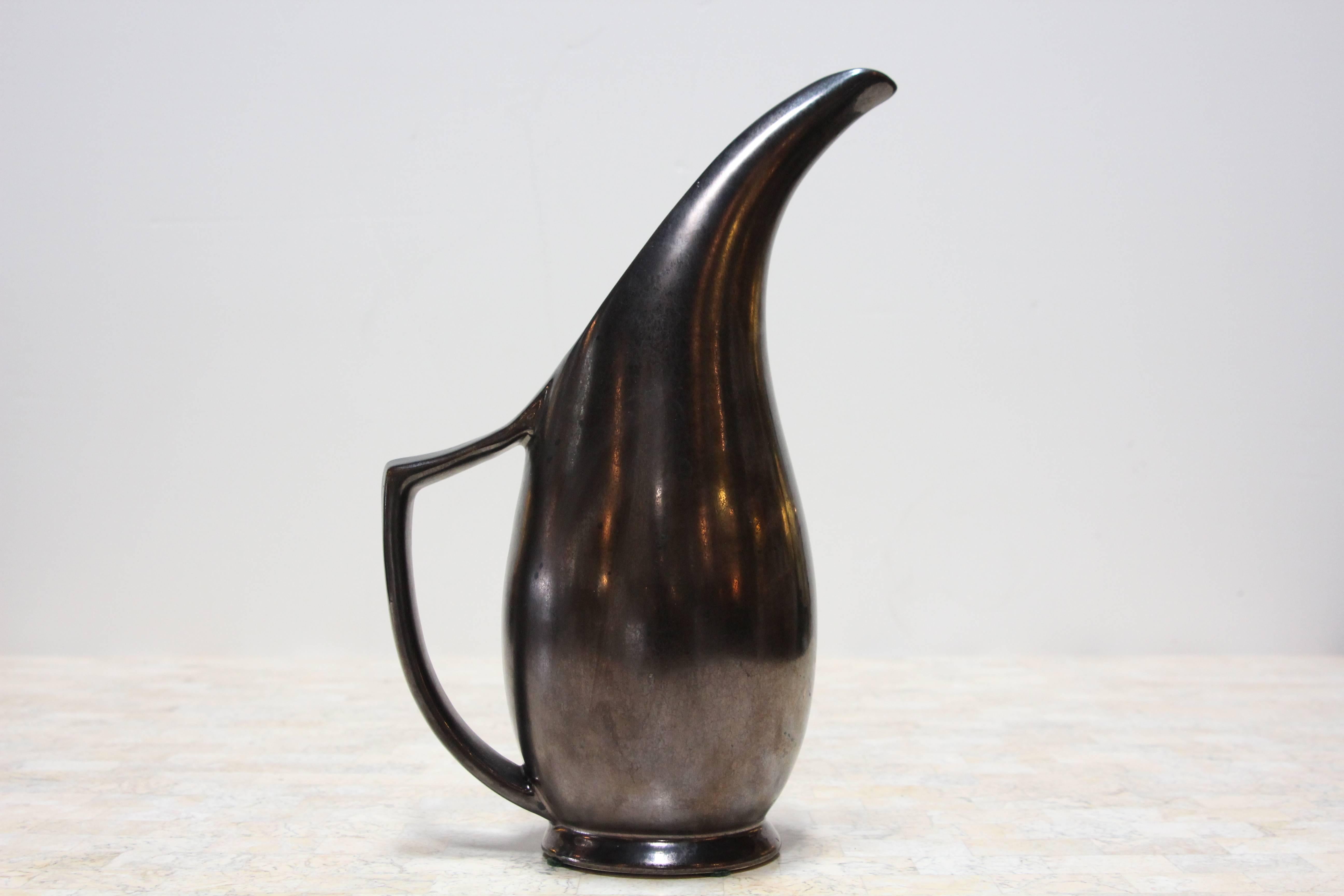 An iridescent black ceramic tall pitcher with a long pouring spout.
The ceramic features golden reflects.