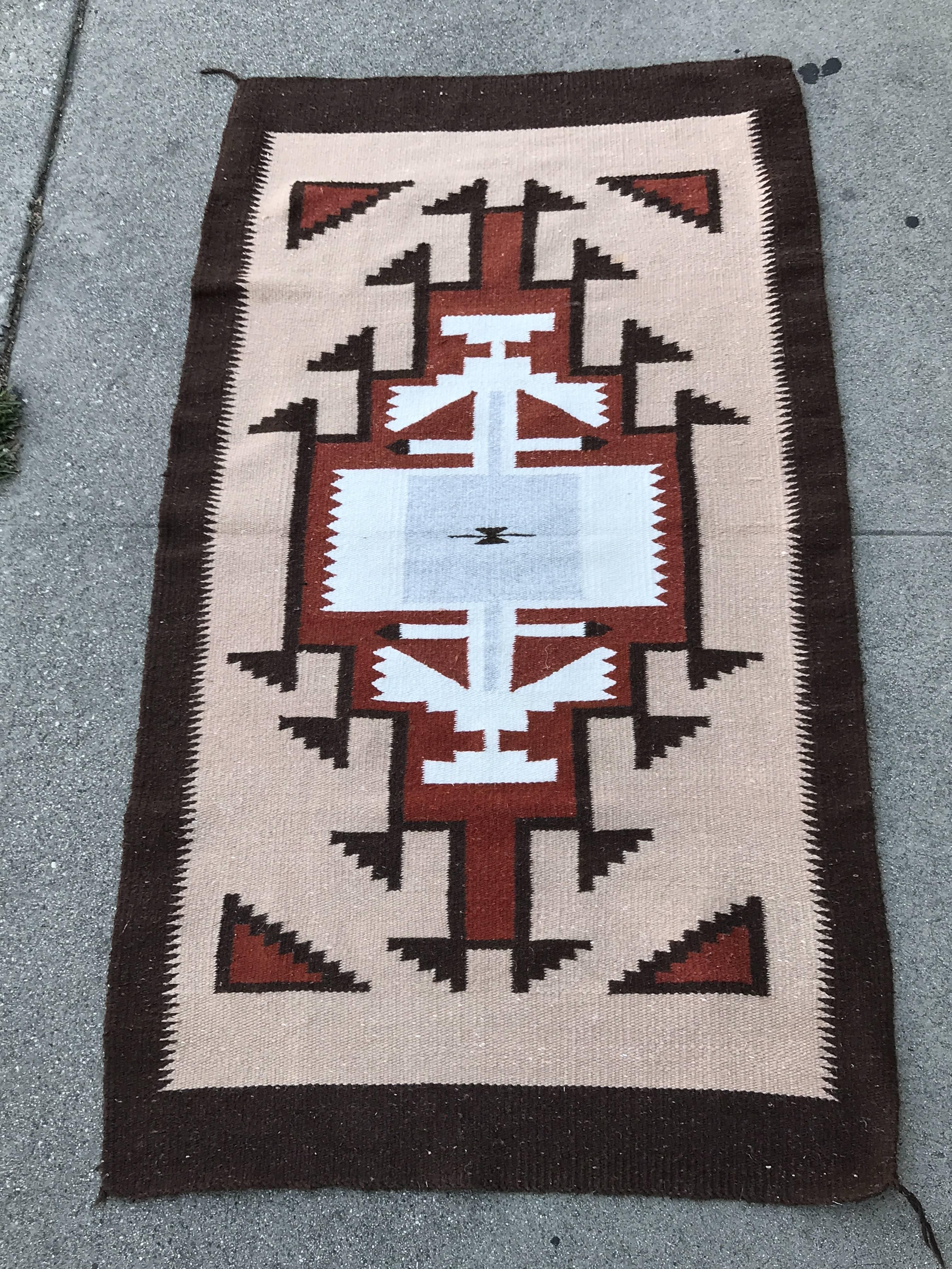 This handwoven wool rug was produced by the Navajo nation sometime during the mid-20th century. The geometric pattern contrasts the use of dark brown line with a white centre and earthy red fill colors.