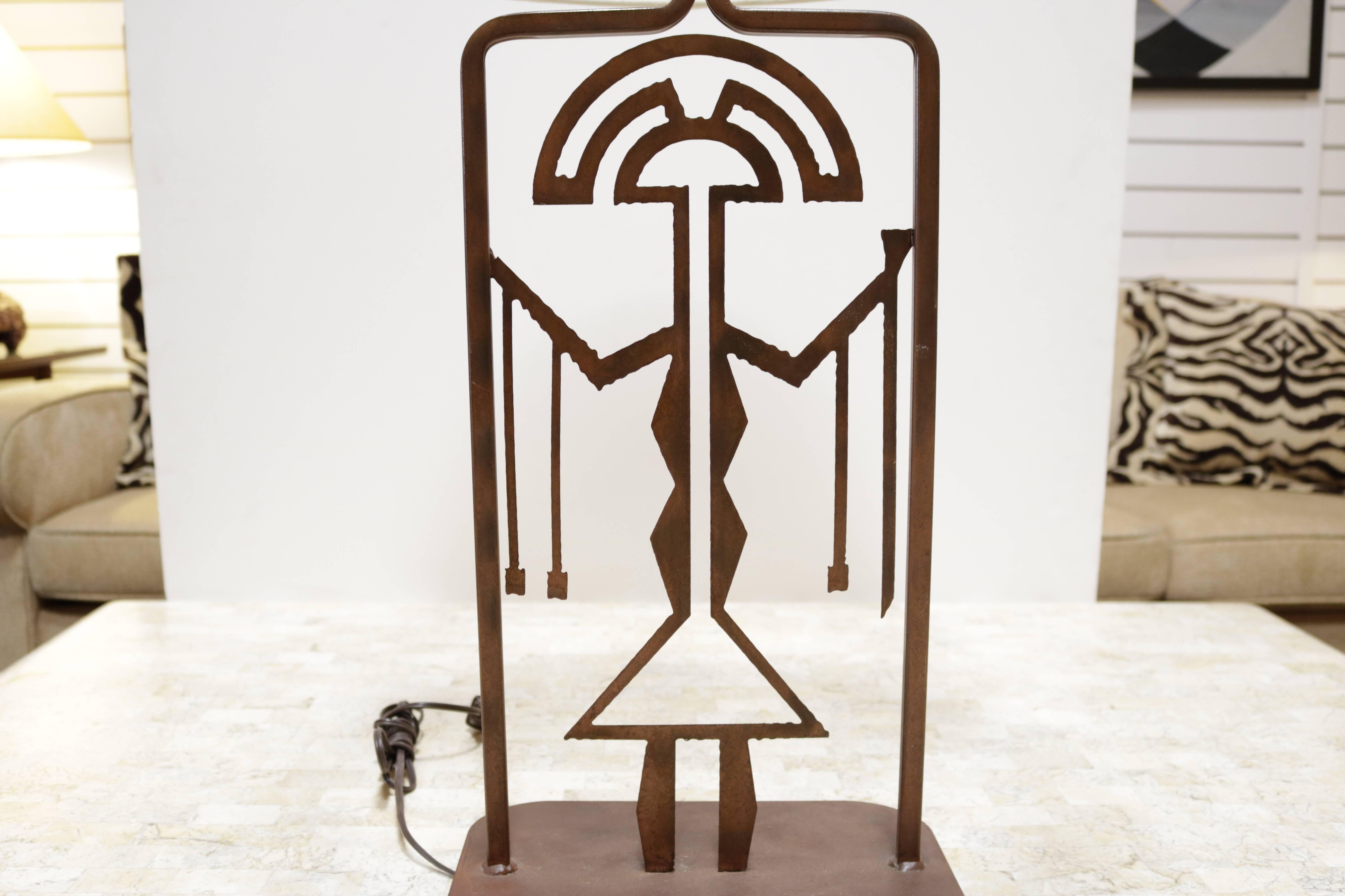 Metal lamp with an intentionally rusted finish. Lamp has a central symbolic figure similar to those used in ancient Latin American art.