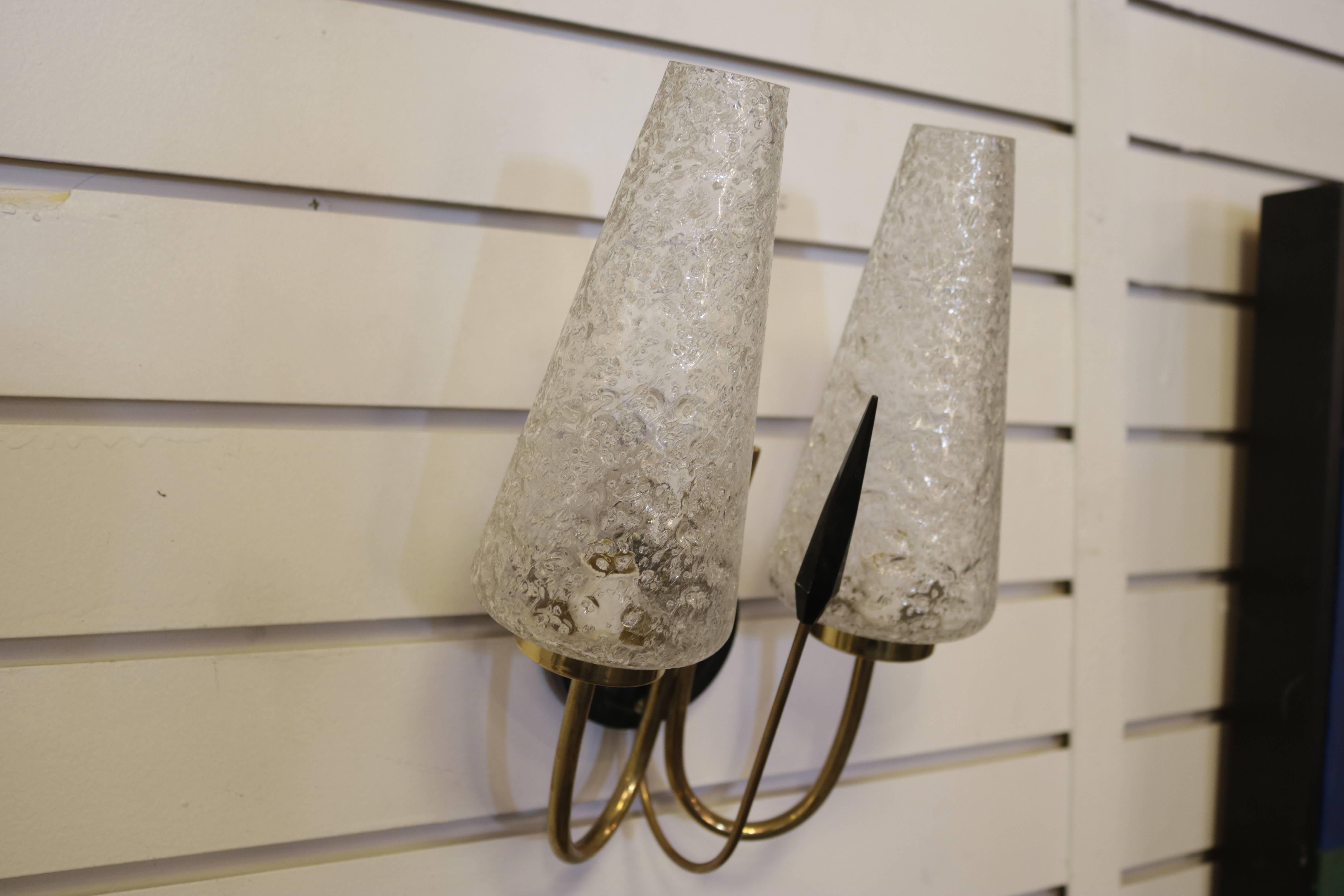 This pair of sconces feature two curved brass stem ended by two textured conical glass shades.
 