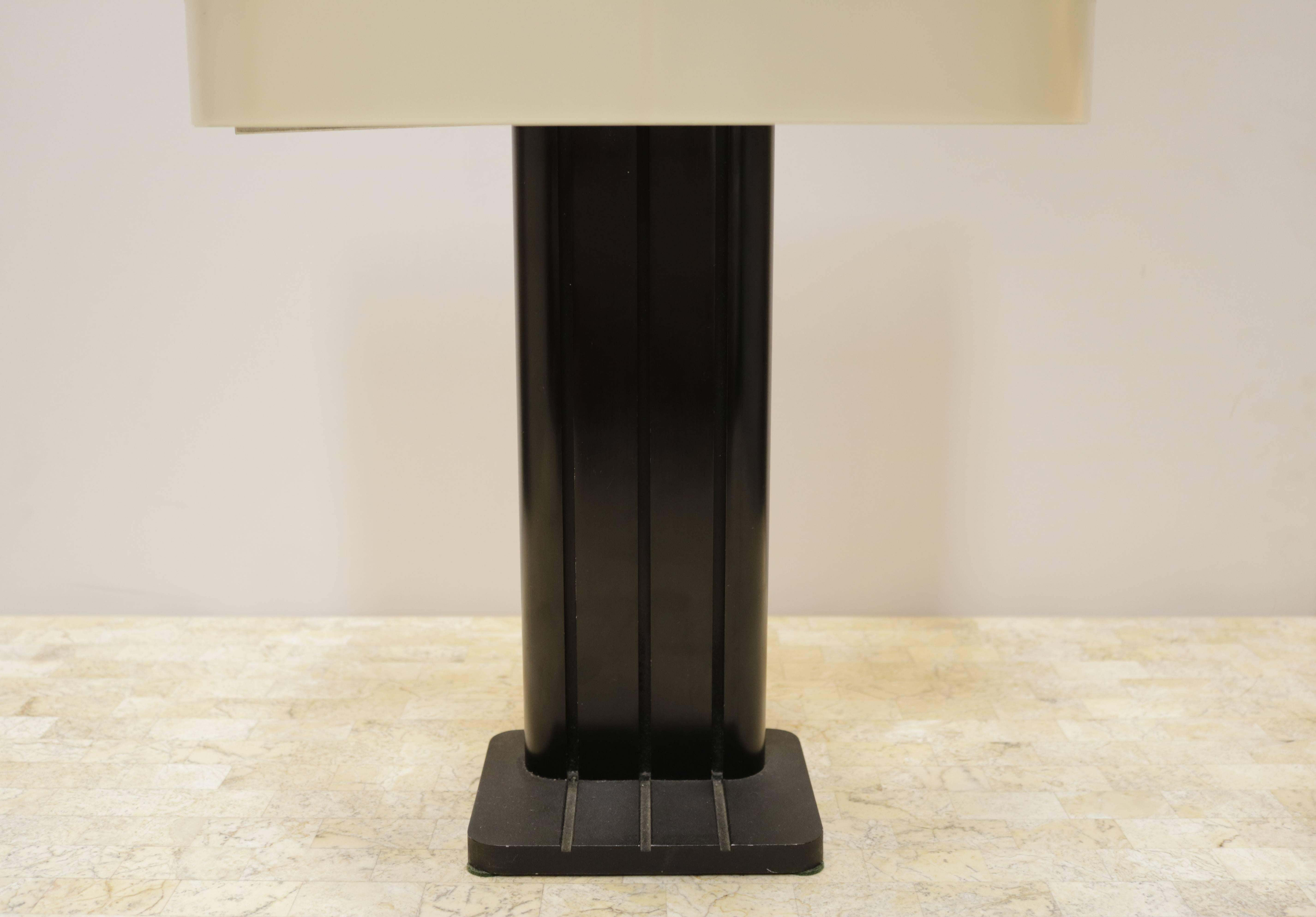 Cream and black, 1970s table lamp has a metal body and plastic shade. The interior of the shade is bisected into two sections with one socket on each side - lamp takes two bulbs.
The half circle shade allows you to place it against the wall on a
