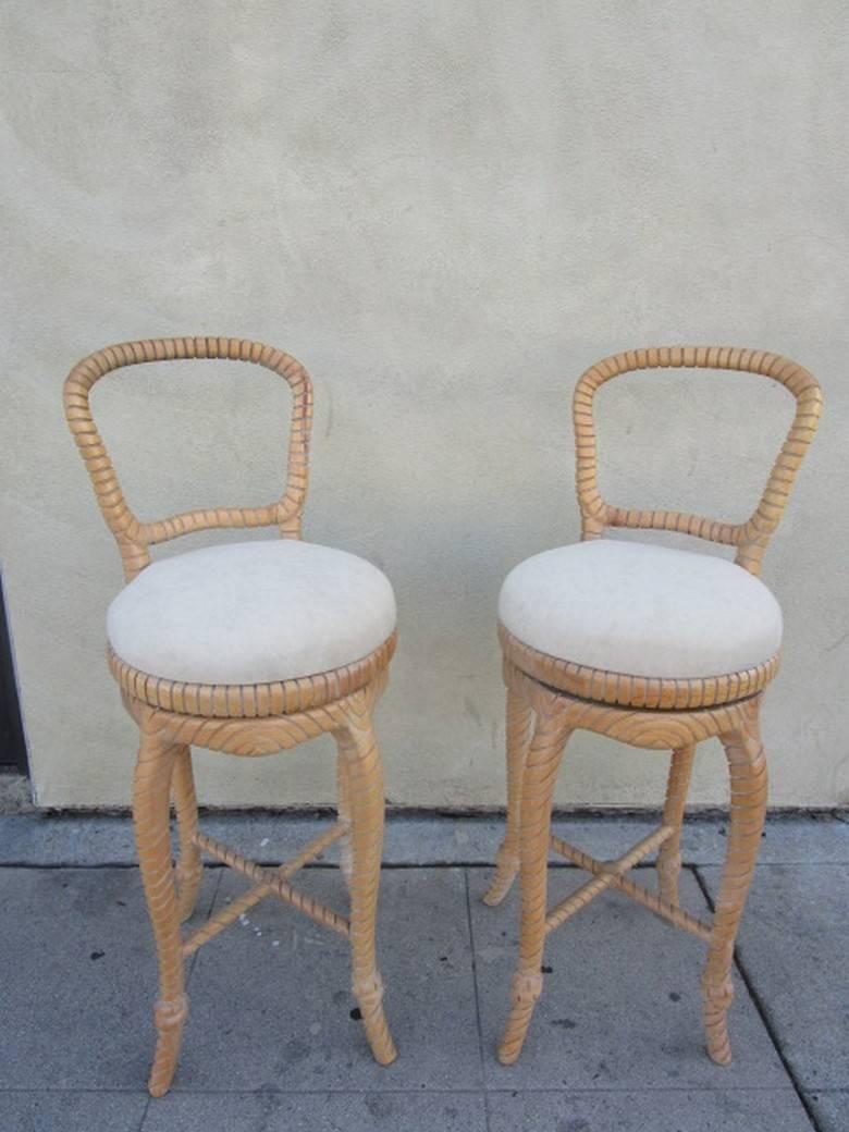 Pair of natural carved wood bar stools with clever knot detail at bottom of each leg. Seats are newly reupholstered in a sand beige ultra-suede fabric and each swivels a full 360 degrees.