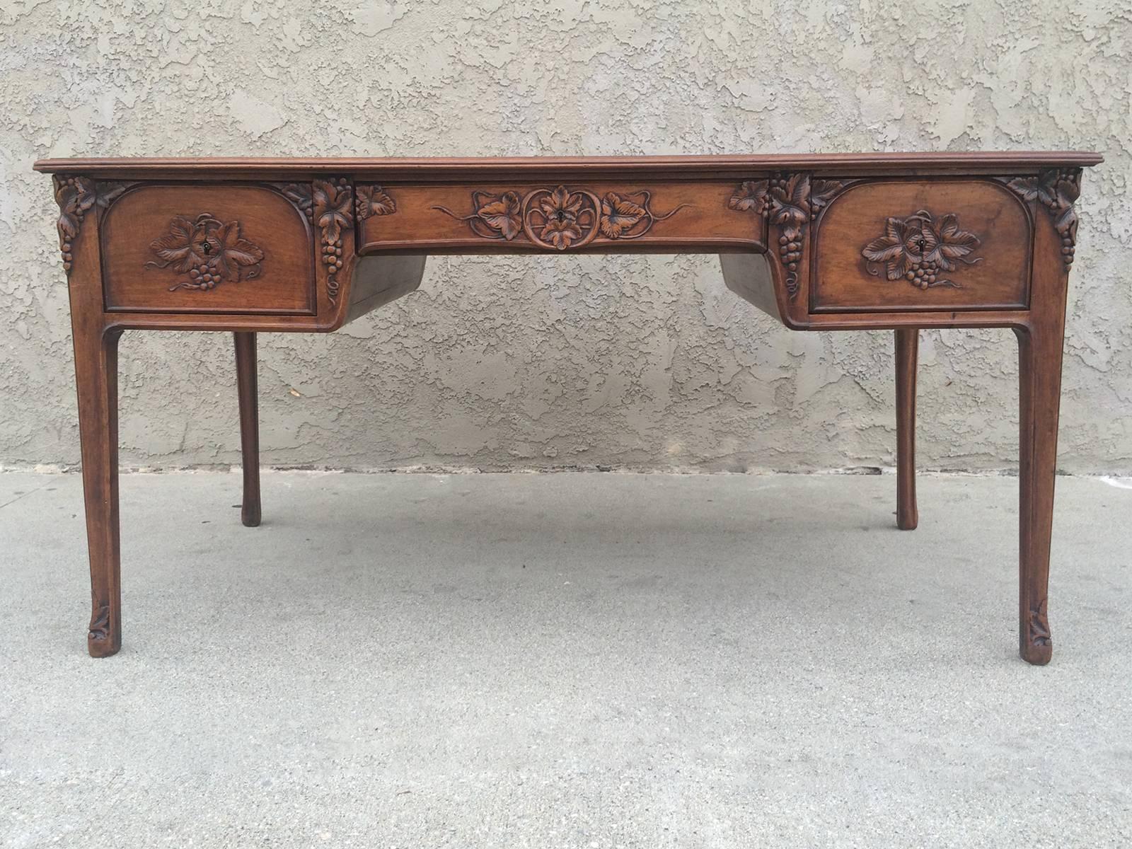 This Art Nouveau desk by Louis Majorelle features carved vine leaves and grapes detailing all around it and at the bottom of the feet.. As such it could be positioned against a wall or in the middle of a room.  The tabletop is inset with leather and