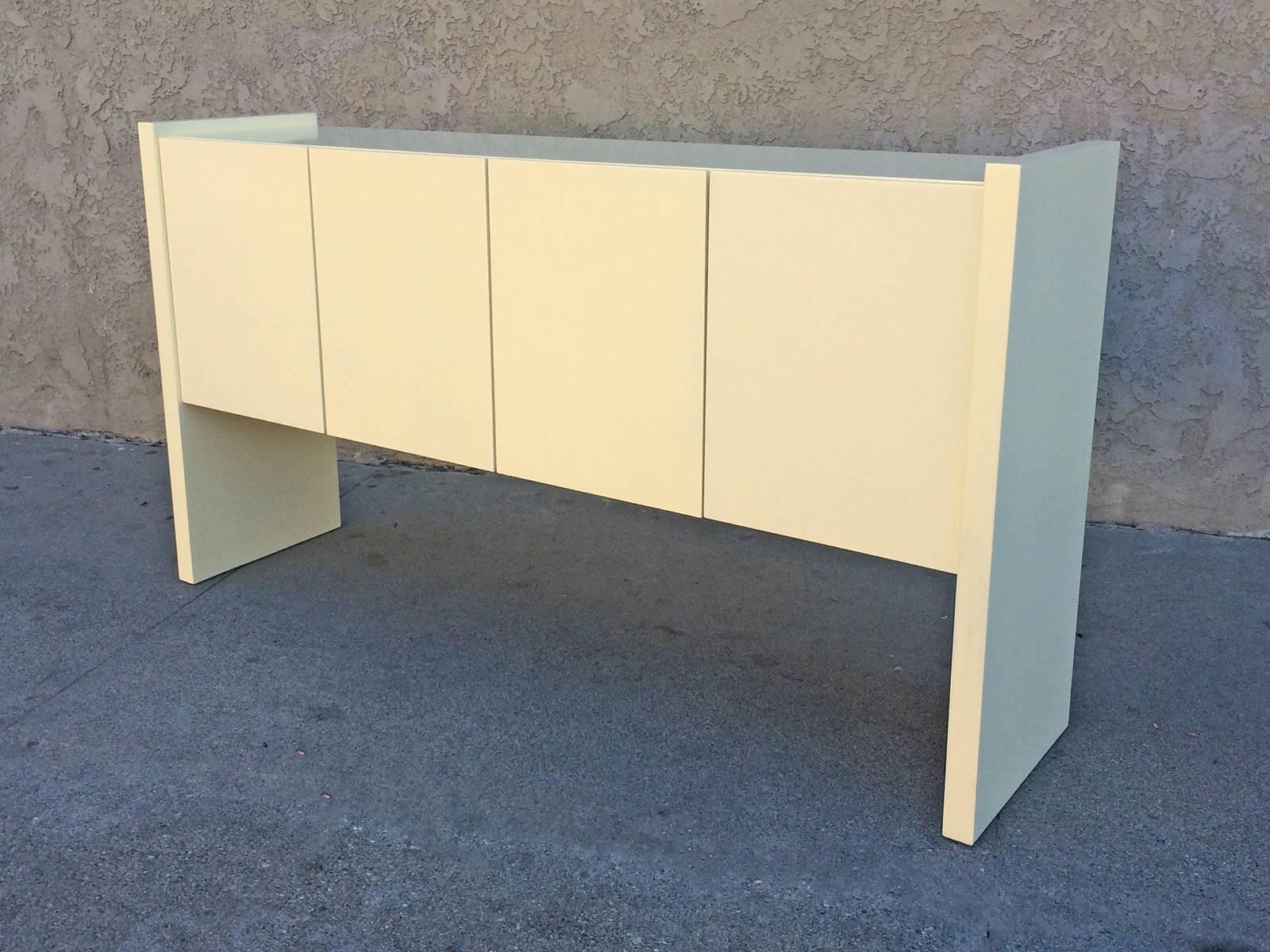 This console designed by Milo Baughman for Thayer Coggin lacquered in a cream/lemon chiffon.  The piece has two sets of double doors concealing adjustable shelved storage on one side (not visible in the image) and two drawers on the other. Great