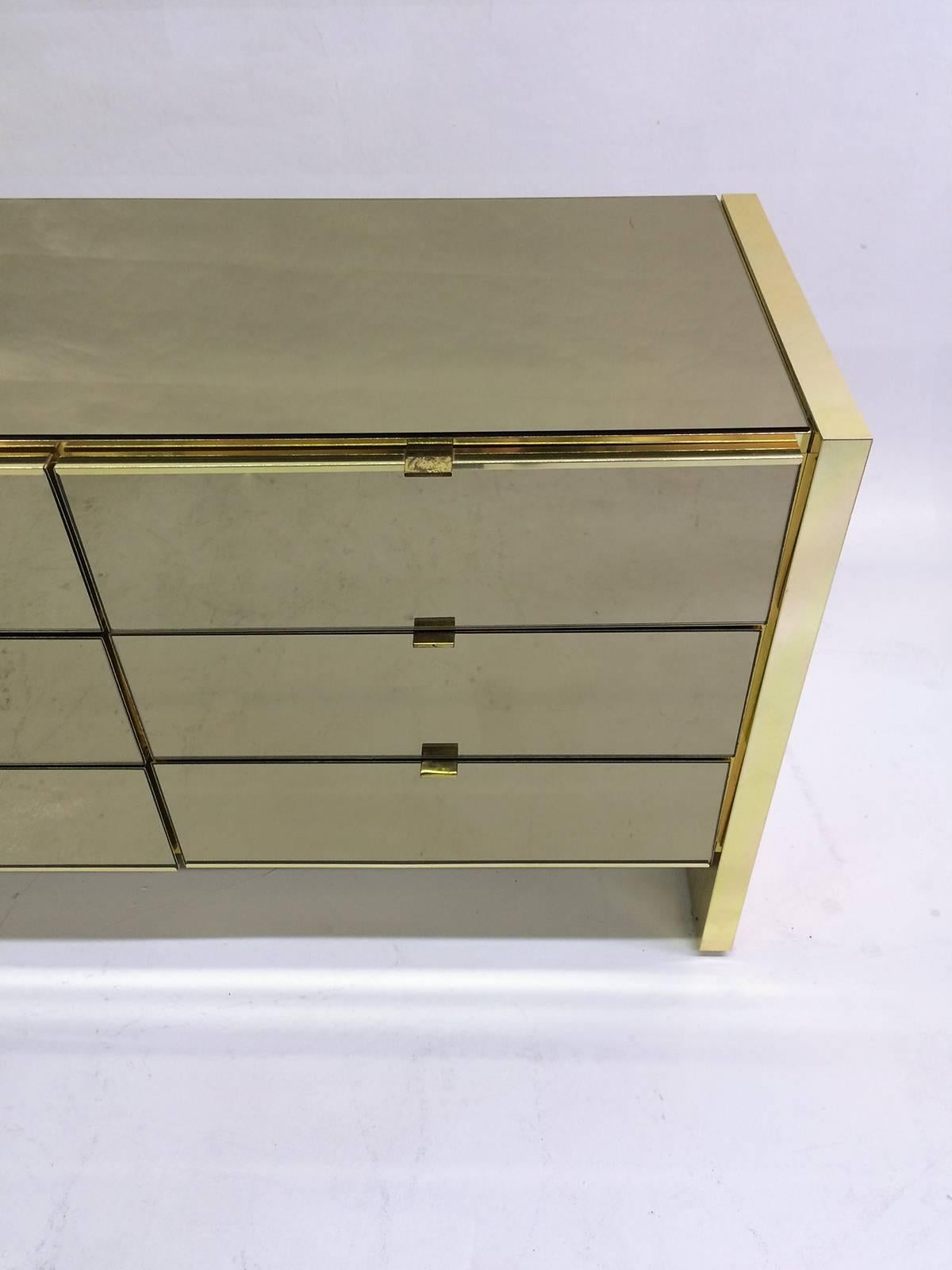 This is a nine drawer dresser made of smoked mirror and polished brass by Ello Furniture which was founded in 1955 in Chicago, IL.