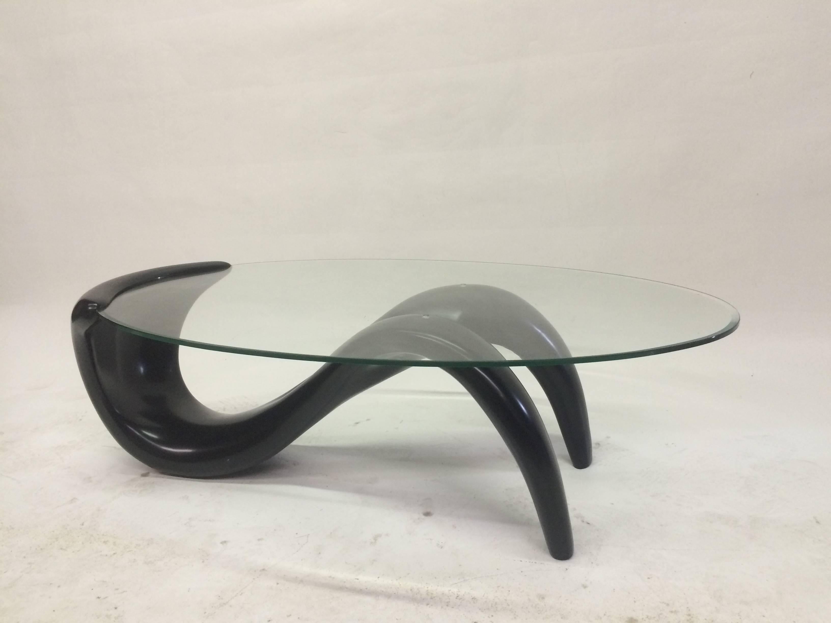  This biomorphic coffee table from the 1980s features an undulating black lacquer finish fiberglass base which hugs the glass surface on one end while supporting it from beneath towards the other end.