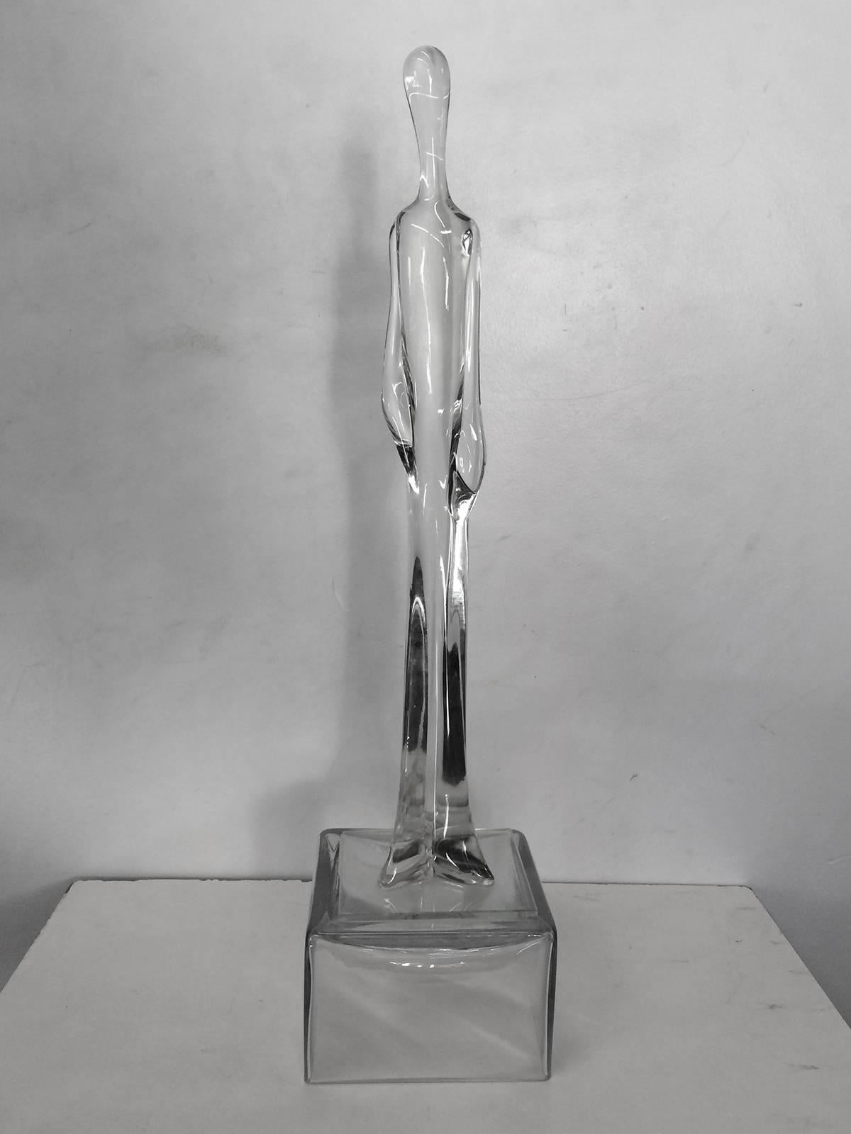Tall and slender glass sculpture which is fluid in form. Although somewhat androgynous, the wide pant legs may define it as being a man.  Sculpture rests on its glass base but, is not attached.  