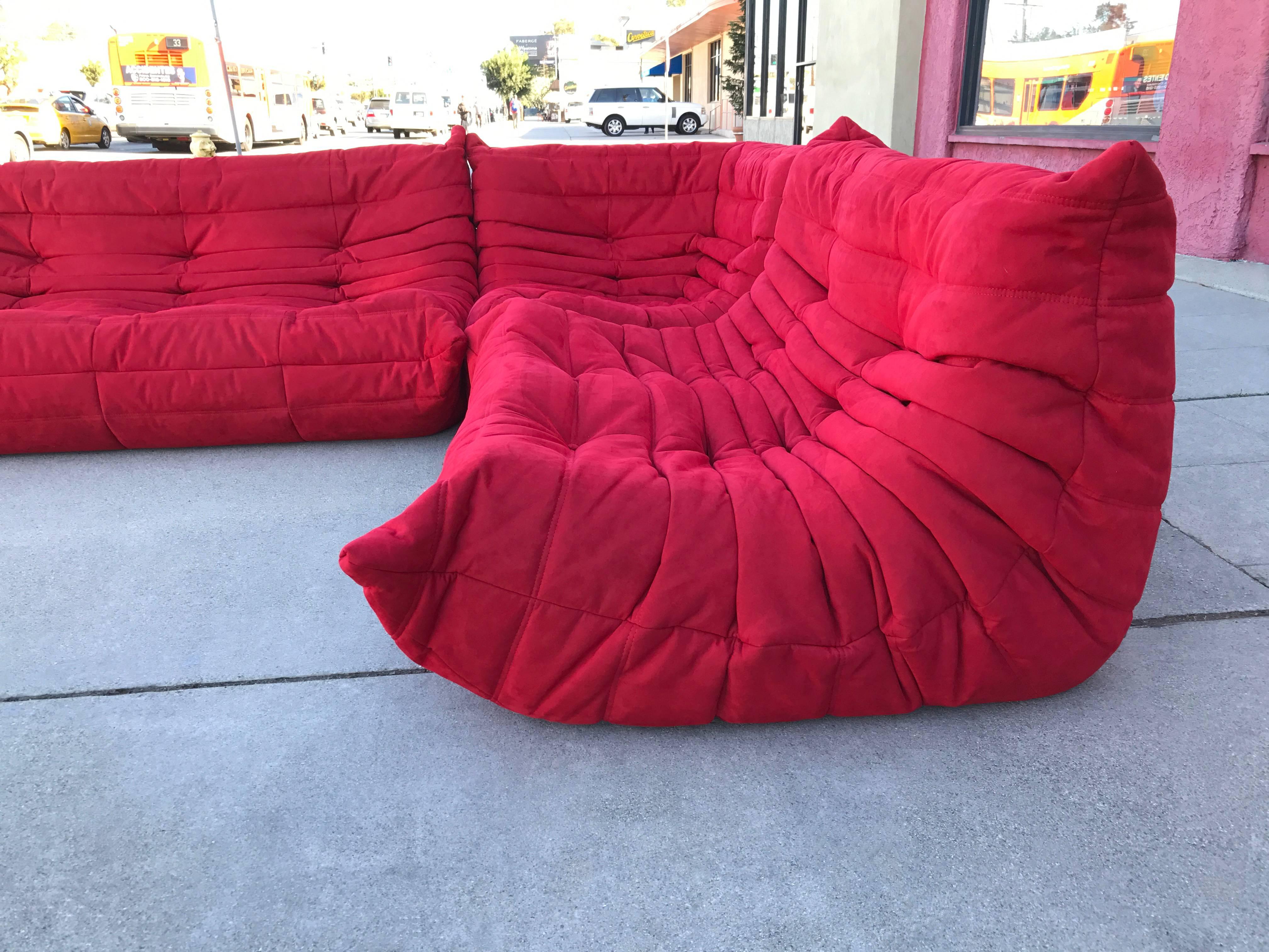 A Ligne Roset Classic, Michel Ducaroy's Togo sofa was first introduced over 40 years ago. This three-piece sectional features an armless couch, loveseat and corner seat in its original red ultra suede upholstery. 
The Toga sofa design is ergonomic