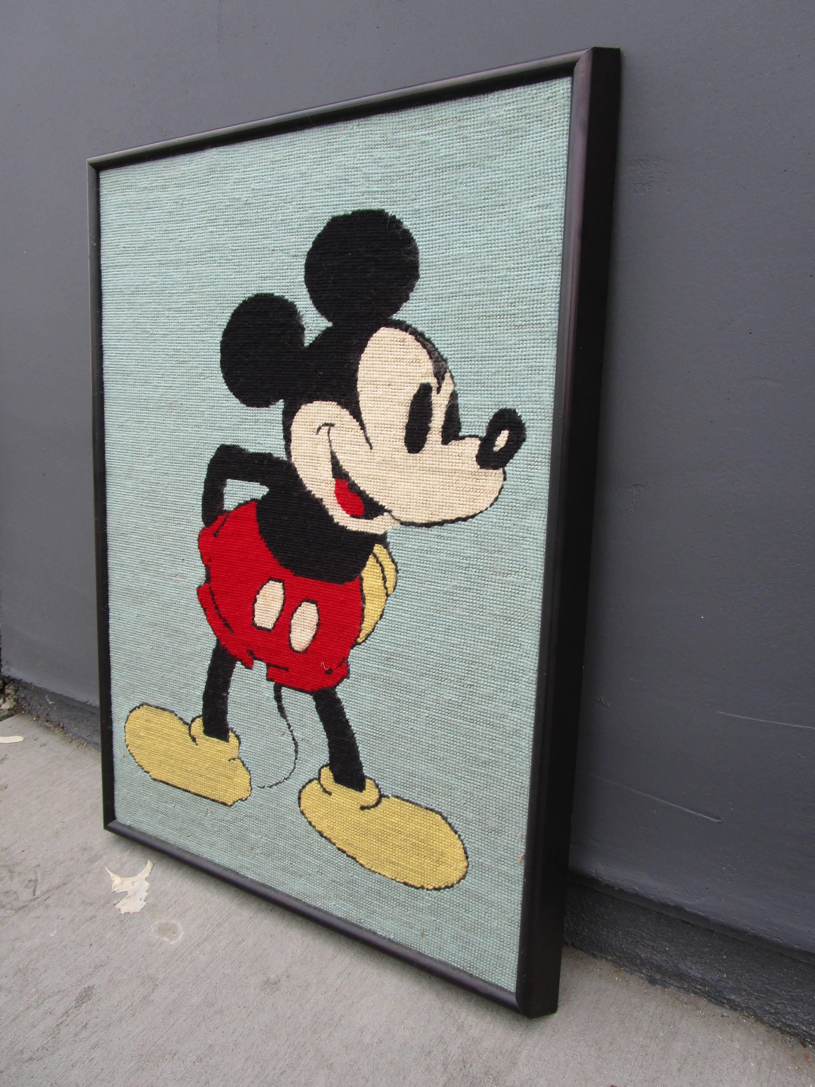 Needlepoint artwork of Mickey Mouse in original black frame. Background is a robin's egg blue.