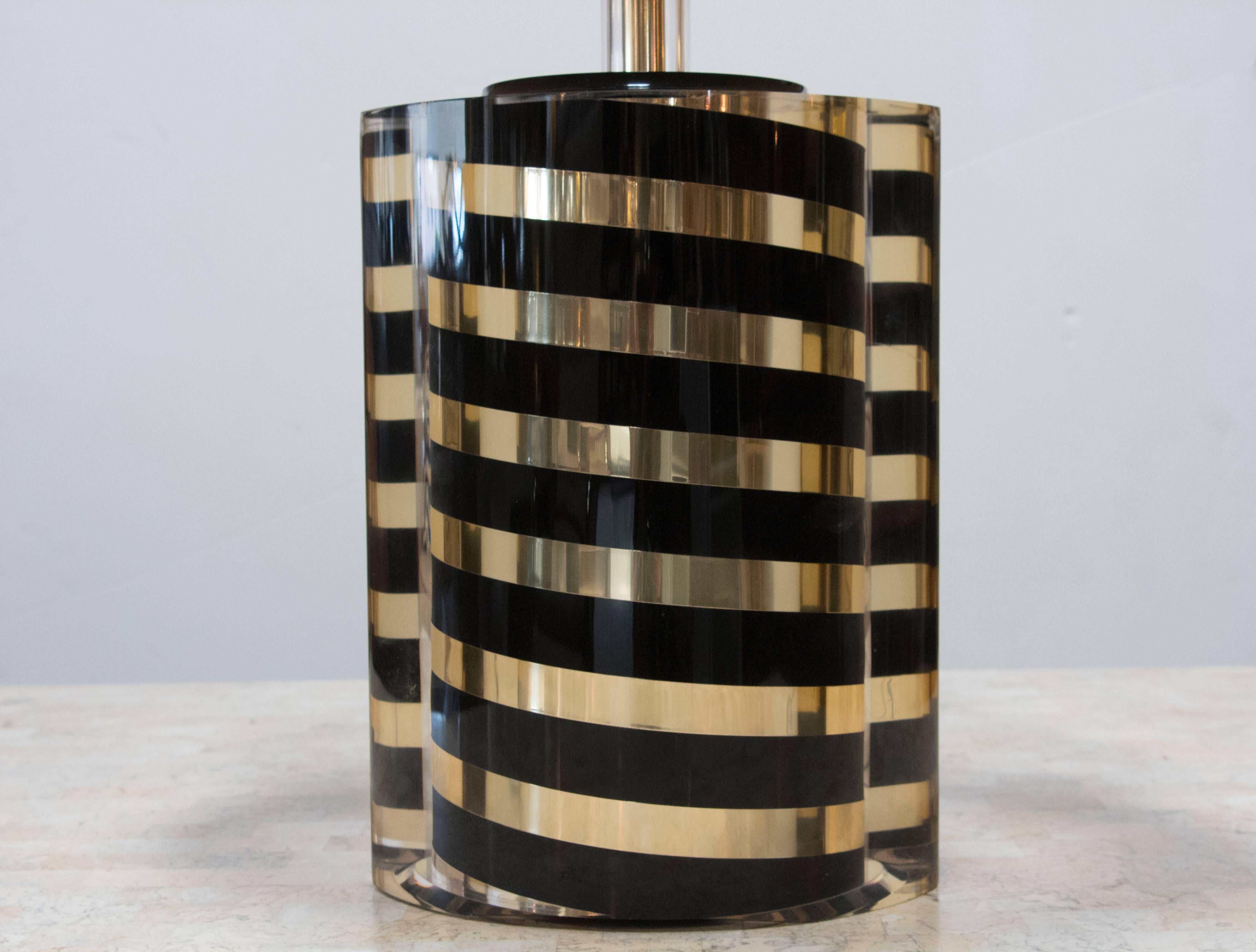Black and gold diagonally striped round base is encased in ellipse or almond shaped Lucite. The difference in the two shapes causes a slight distortion in the appearance in photos - what is really a reflection appears as if the outer surface is