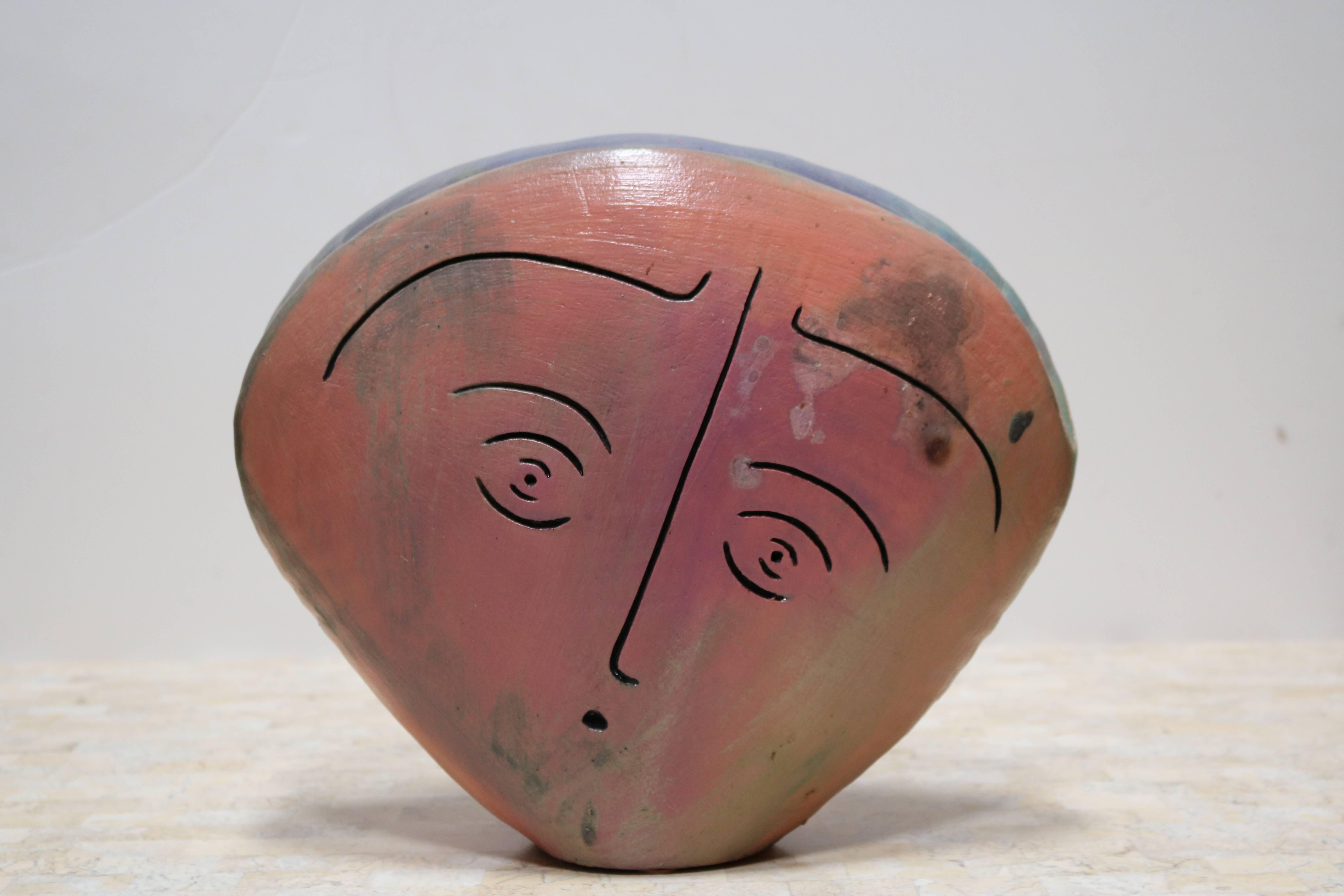 Ceramic sculpture with face carved into either side in shades of coral and dusty pink with aquamarine and even lavender at the very top. 
 Sculpture cannot be used as a vessel - though it does come to somewhat of a cleft, there is no opening for