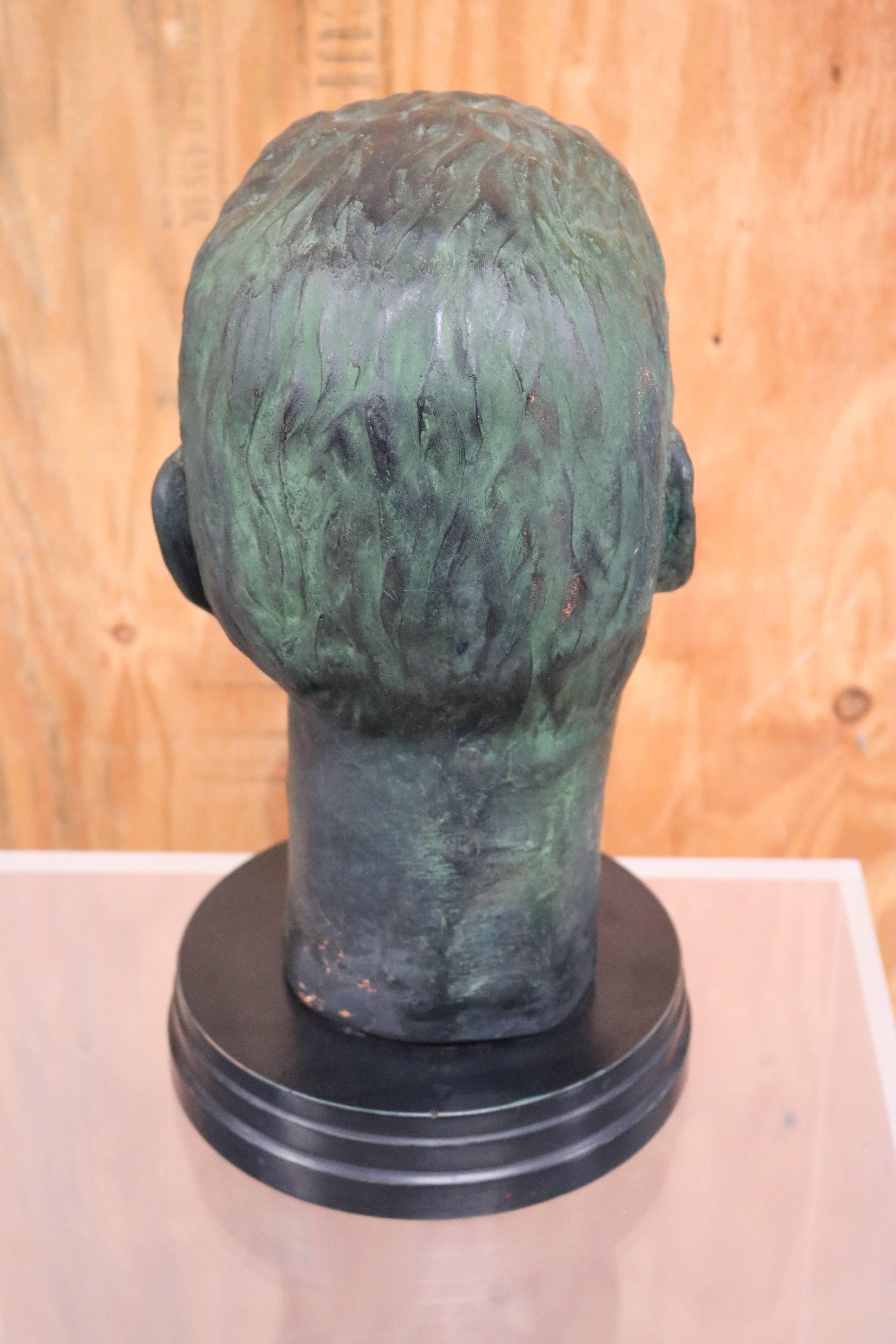 Julius Caesar head sculpture rendered in bronze with a verdigris finish. It sits on a round black wood base.