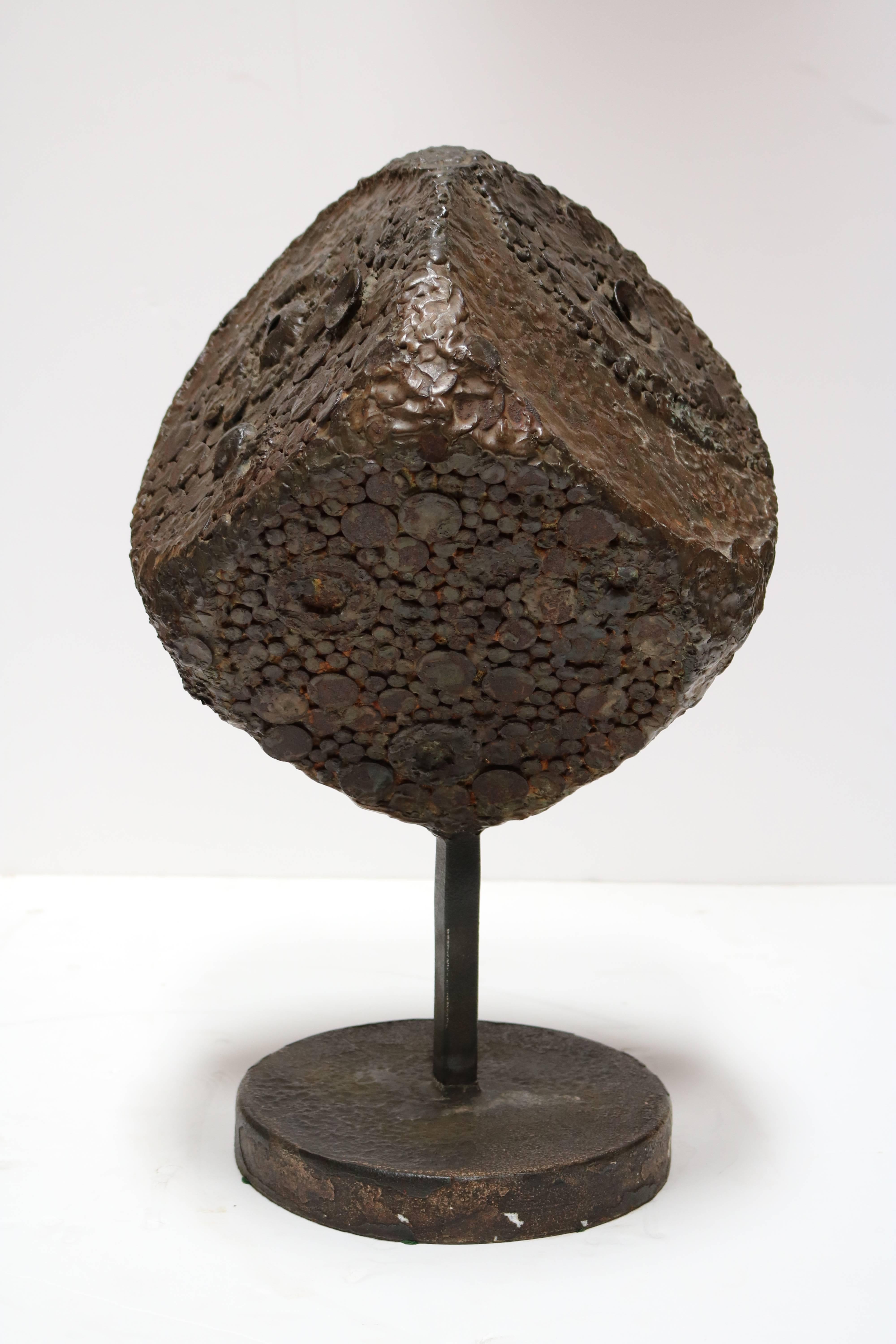 This fascinating sculpture rendered in bronze is composed of a large, highly textured cube supported by a rectangular stem and a circular base. The fascinating, hand-wrought surface of the cube changes from every perspective and light giving the