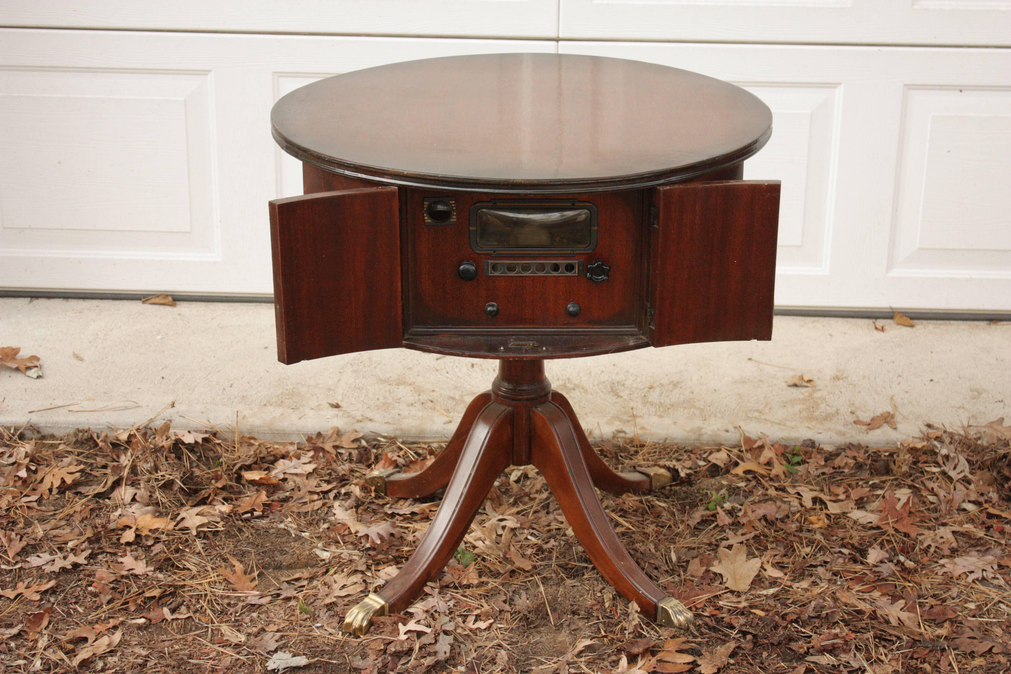 1930s English round stained mahogany faux cabinet doors pedestal base table with brass lion head pulls and brass claw feet on casters. Front doors open to faux antique radio controls and a looking glass. Beautifully polished and stained mahogany