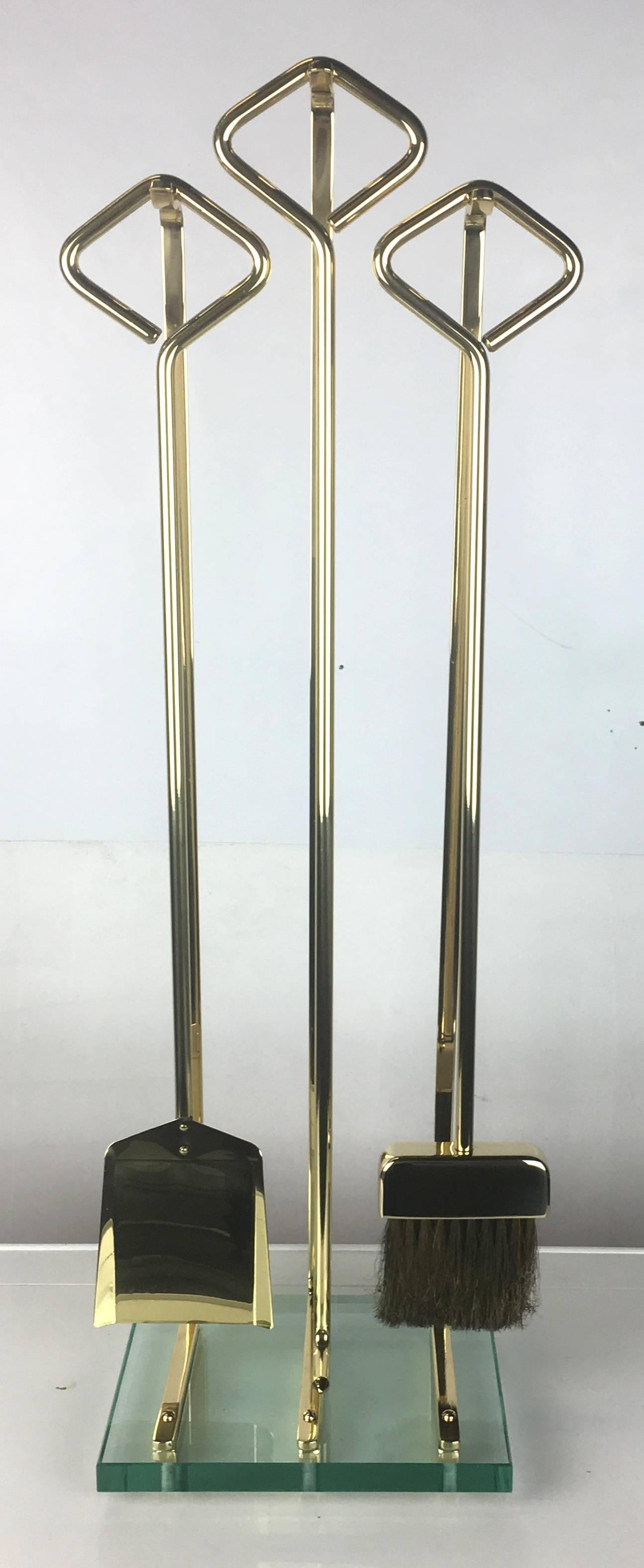 Finely crafted solid brass set of fireplace tools in the style of Fontana Arte. The set has been painstakingly restored; professionally polished, lacquered, and presented in as-new condition. The set consists of a thick glass base sitting three