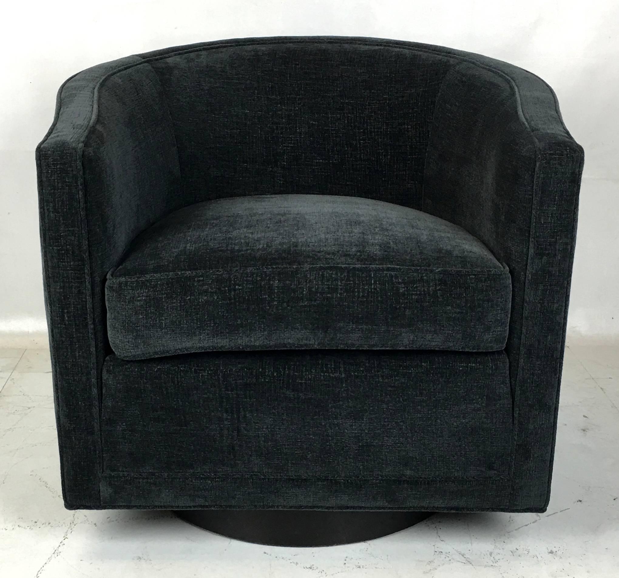 Classic swivel chair by Dunbar raised on a ebonized walnut drum base. The chair has been meticulously restored and reupholstered in a heavy weight dark grey textured chenille.  All work done with painstaking attention to detail at our in-house