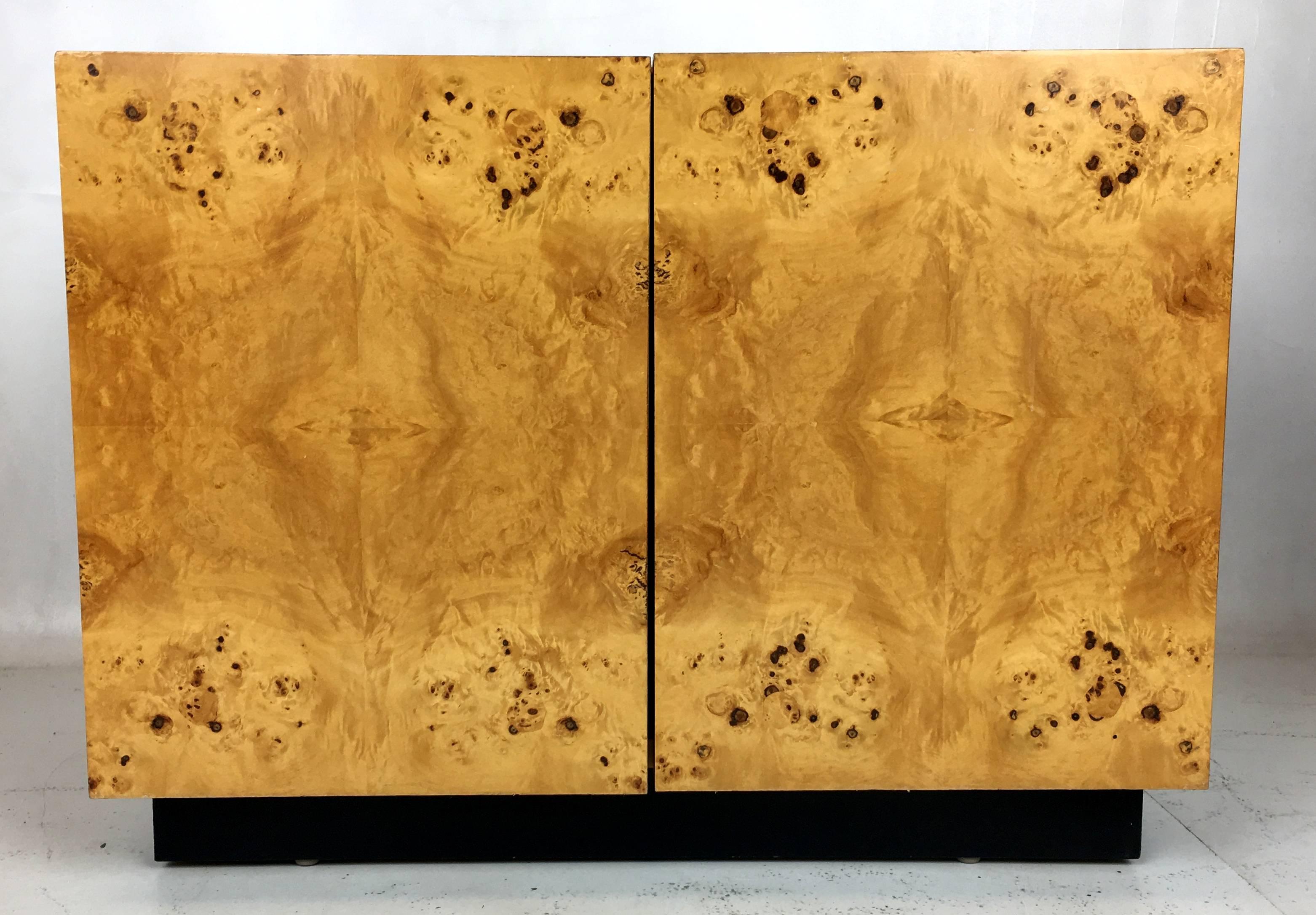 Cool pair of olive burl nightstands raised on black laminate plinth bases. Both chests have a pair of slab doors with magnetic catches and divided shelves on the interior. This pair will work equally as well as a pair of lamp tables.