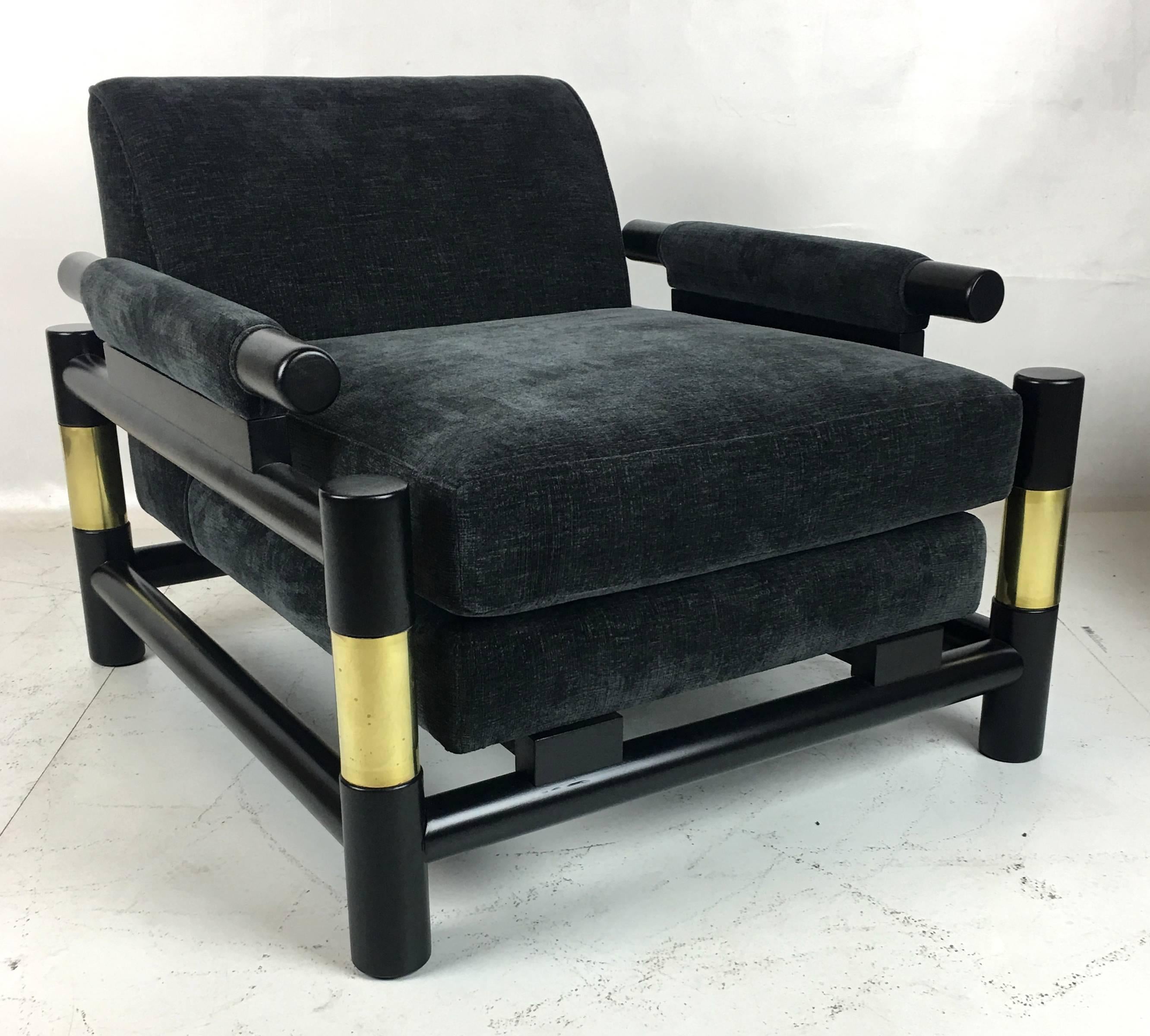 Striking pair of ebonized open frame lounge chairs in the style of Paul Laszlo with large diameter dowel frame. The pair have been painstakingly restored; refinished, brass polished, and reupholstered in luxurious charcoal grey chenille. Highest