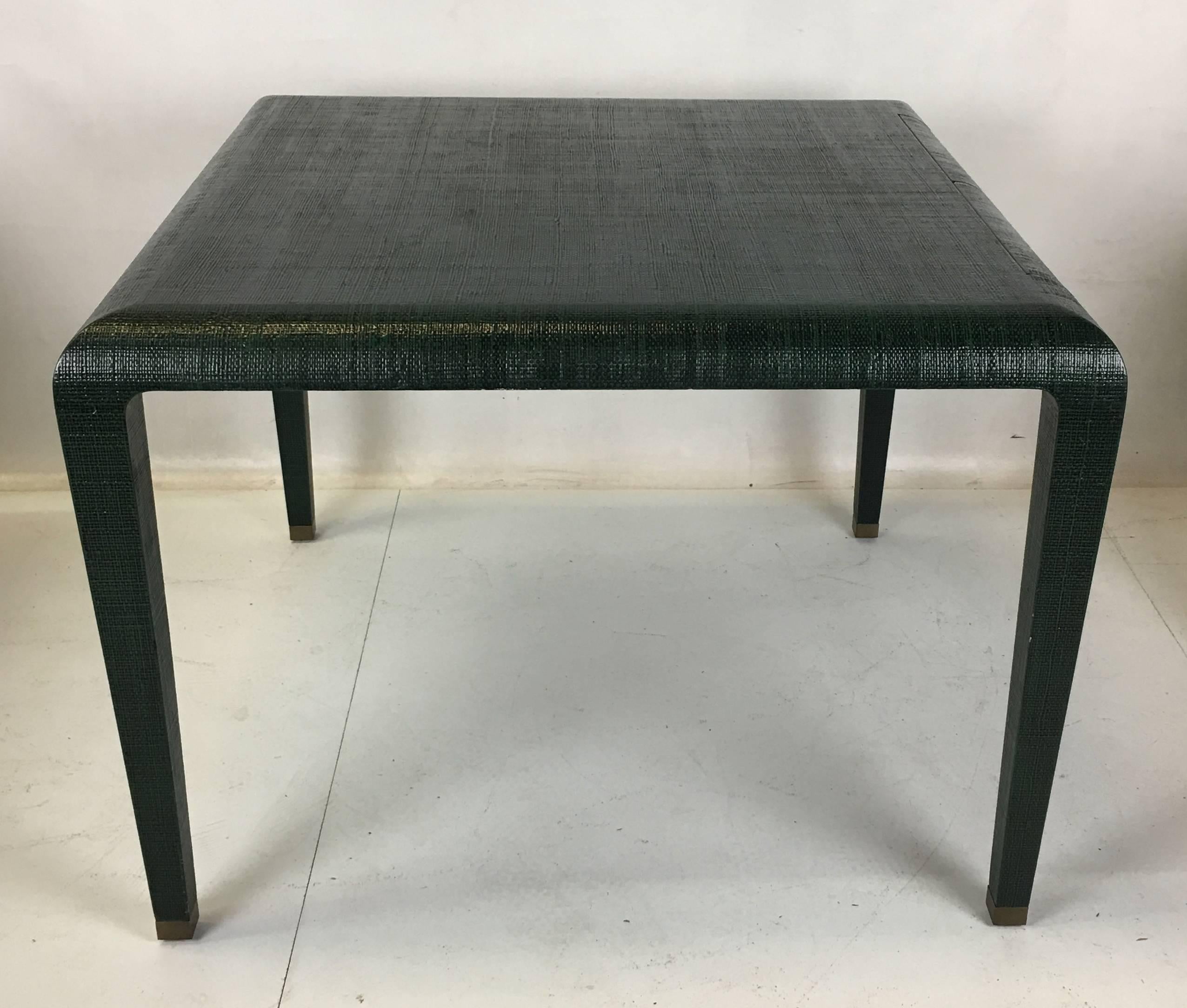 Superbly crafted games table clad in lacquered Raffia with two pencil drawers on one side. The tapered square legs terminate in heavy brass sabots. The Raffia is lacquered in hunter green with black undertones. Van Horn's quality and workmanship is