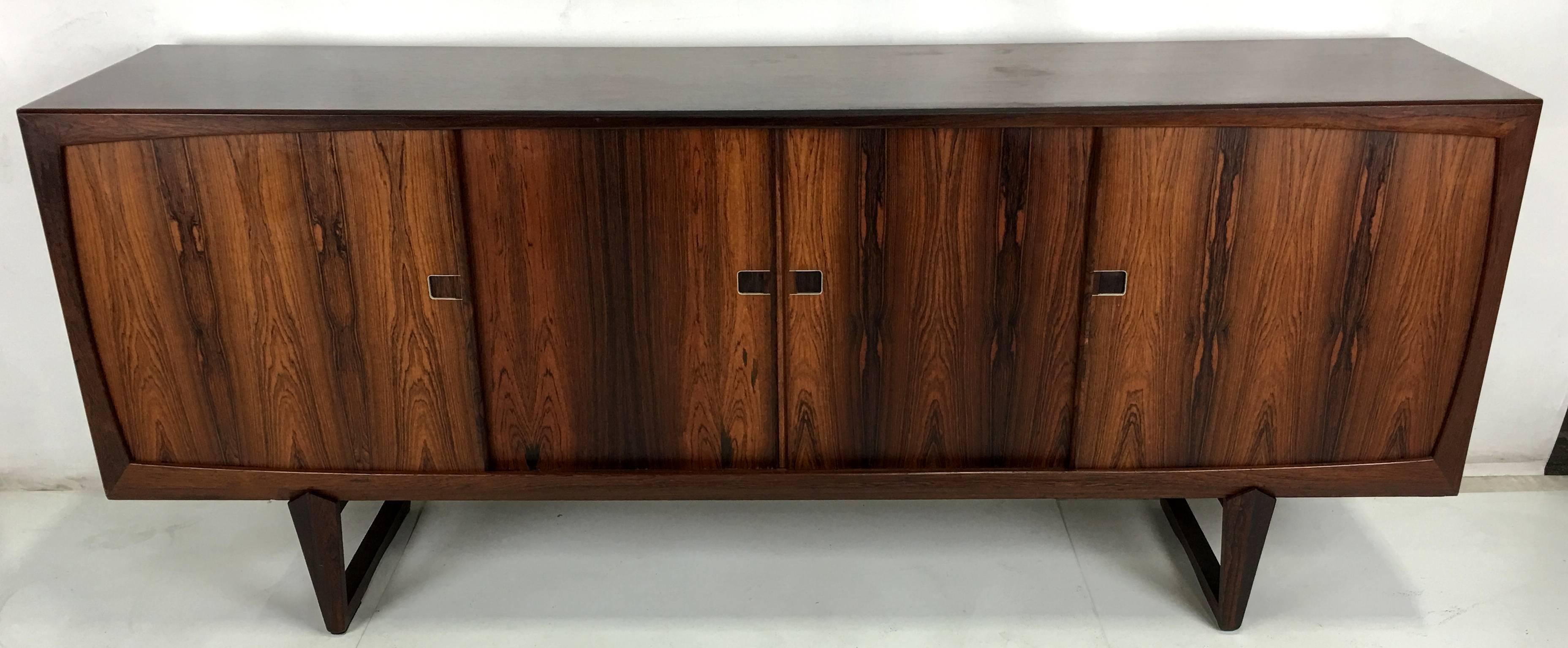Vividly grained and super quality Danish rosewood credenza with sculptural sled style base. The cabinet is superbly crafted and the rosewood finger pulls are lined with stainless steel. The two end compartments conceal adjustable shelves and the