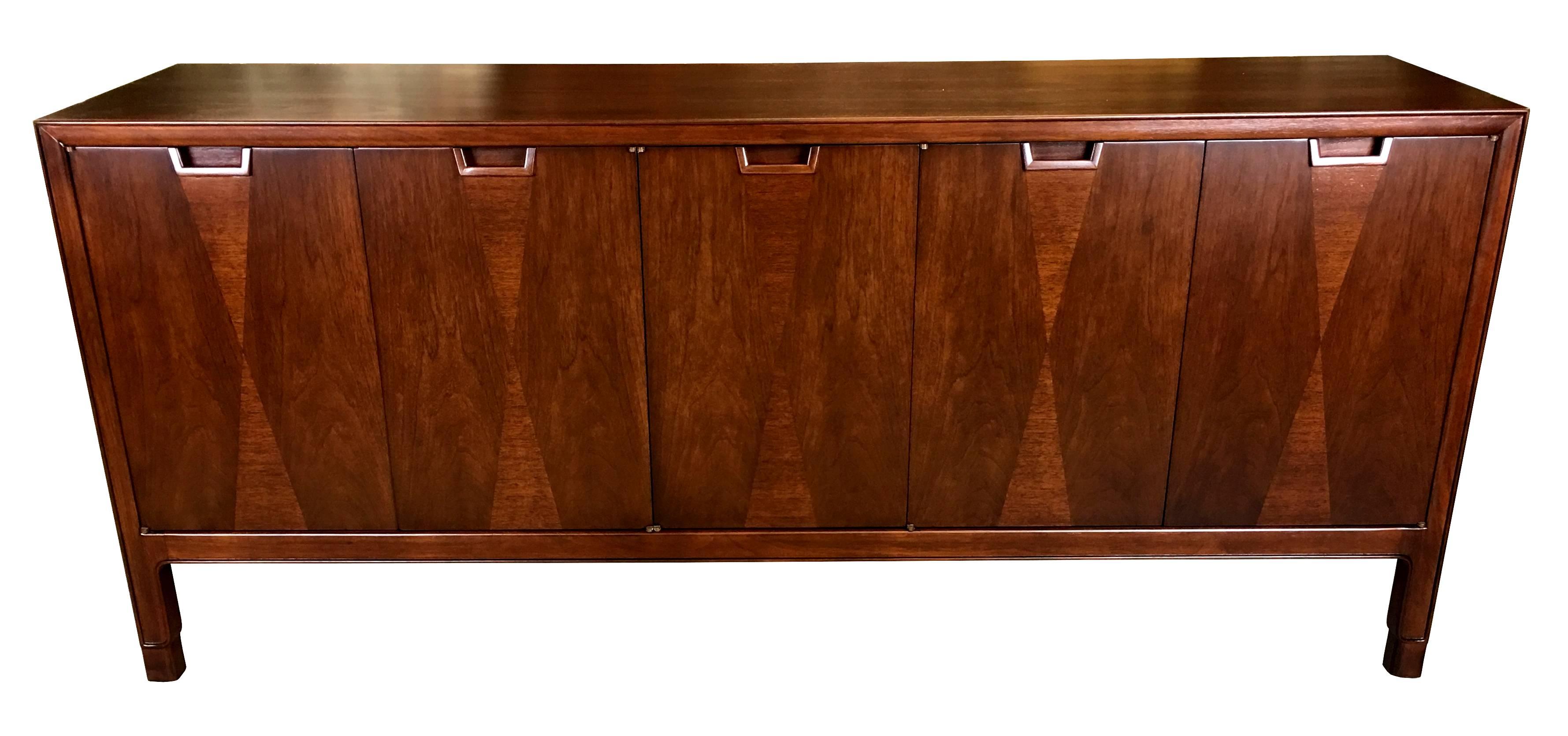 Finely crafted walnut sideboard or buffet by John Stuart, New York. The cabinet features inlaid diamond pattern on the doors, which conceal walnut-fronted pullouts on one side and a recessed shelf on the other half. The piece has been painstakingly