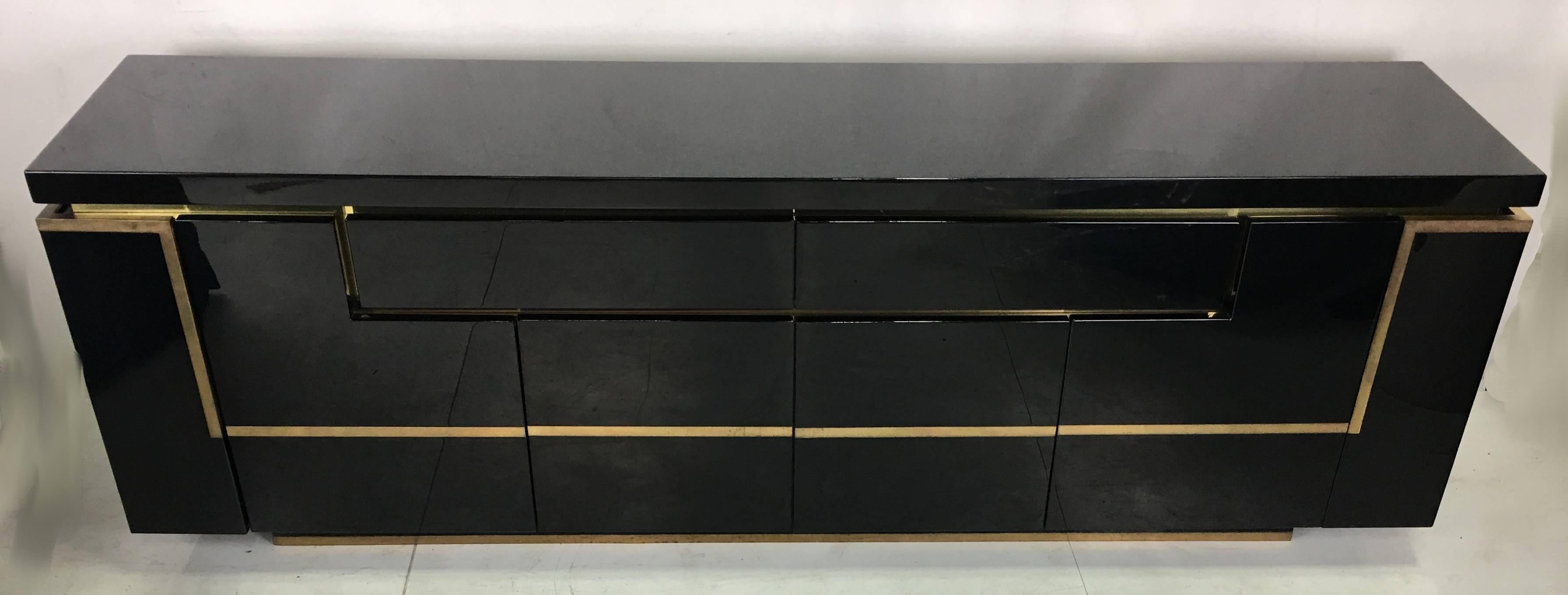 Luxurious sideboard in Seventies jet set style by Jean-Claude Mahey.  Lacquered high gloss front and top in black with brass applications.  The sideboard has two drawers, four doors and two bar doors at the sides.  The piece is in excellent original