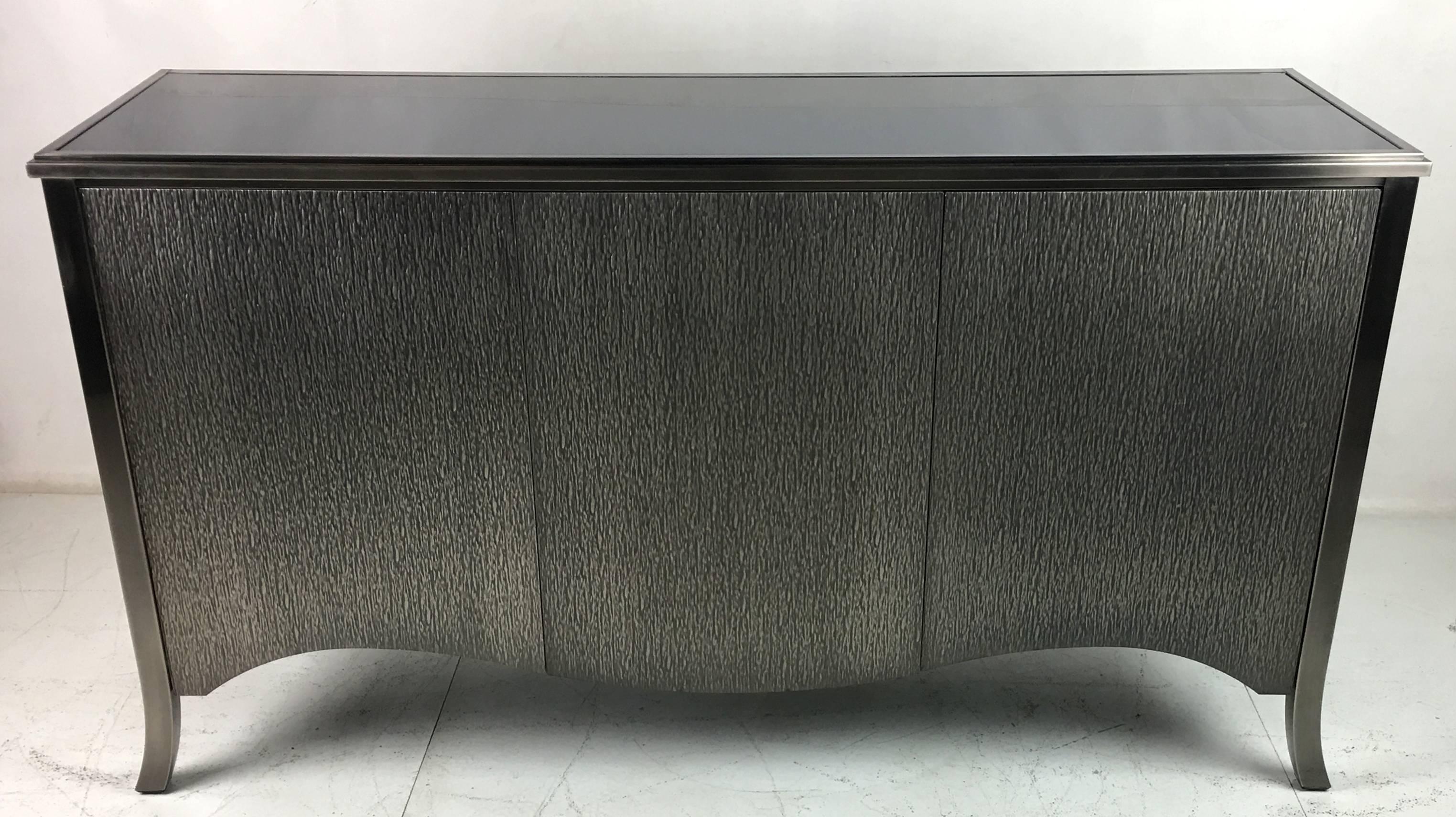Textured Steel clad cabinet with steel cabriole legs by Mastercraft. The three-door buffet has an inset black glass top and adjustable height interior shelves. The door fronts and sides are clad in heavy-gauge embossed steel. Top quality