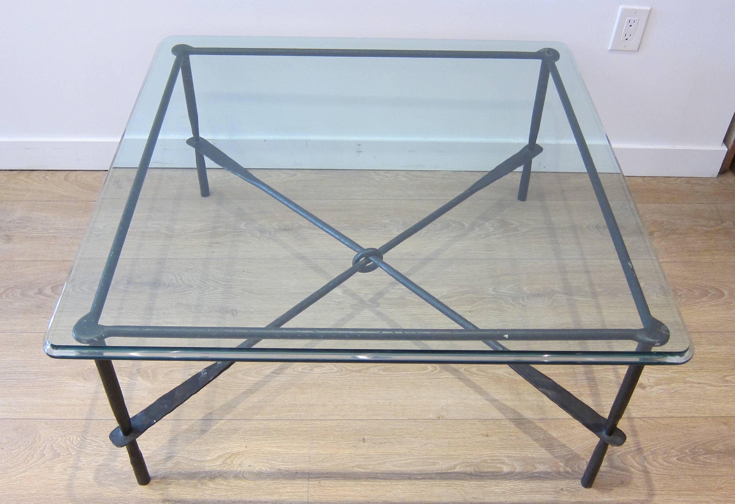Giacometti inspired coffee table. Hammered and forged iron with oil rubbed bronze patina. Beveled edge clear glass top. Cross beam stretcher knotted at the center. Very good condition, consistent with age and use. 
For additional questions regarding