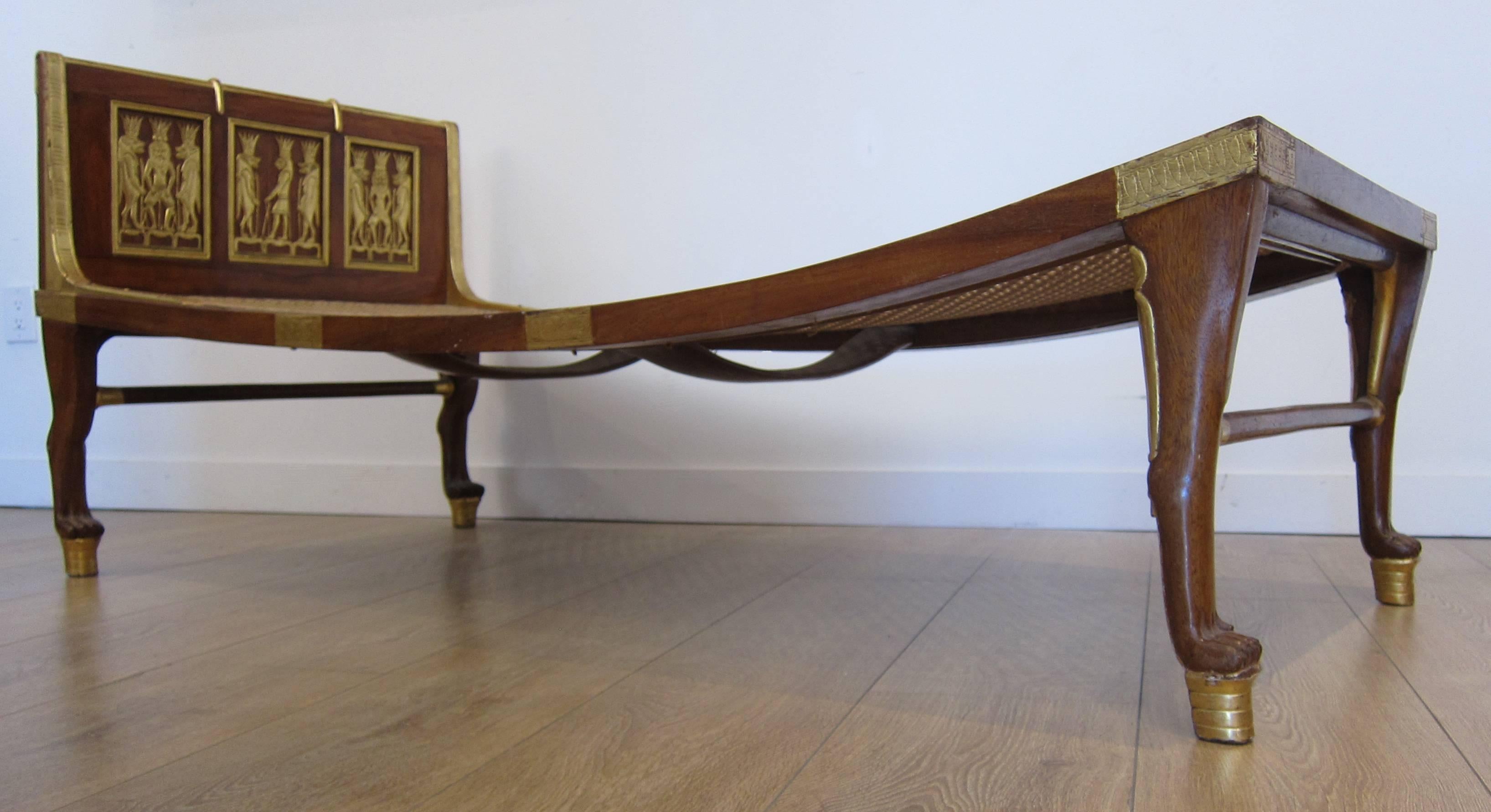Absolutely beautiful Egyptian revival style daybed or chaise longue. Finely carved mahogany legs in the form of lion paws. Well executed parcel gilt artworks displayed on the headboard, sides and foot board of the bed. Mattress is made of plaited