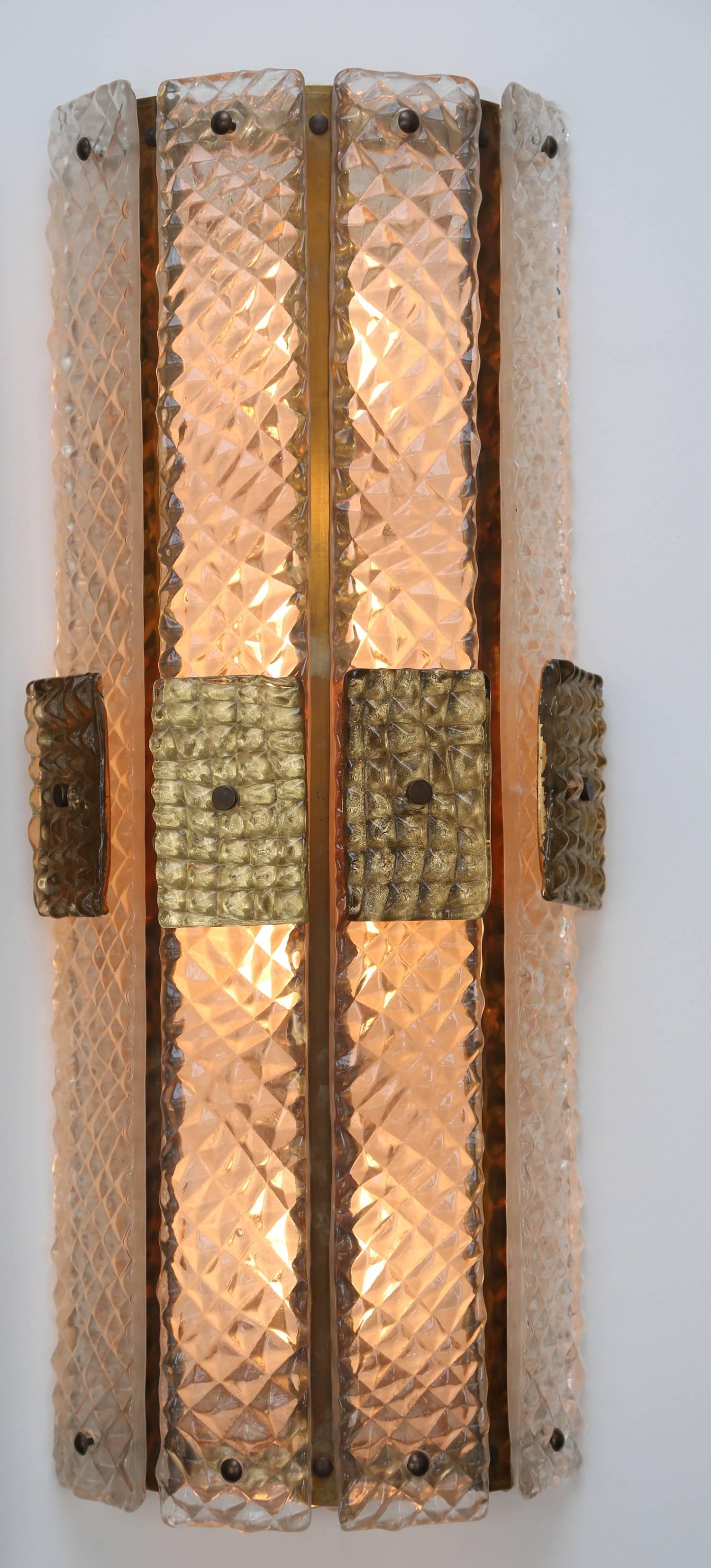 A large pair of mid-century modern style, clear and gilded, textured Murano glass wall sconces with brass accents.
 