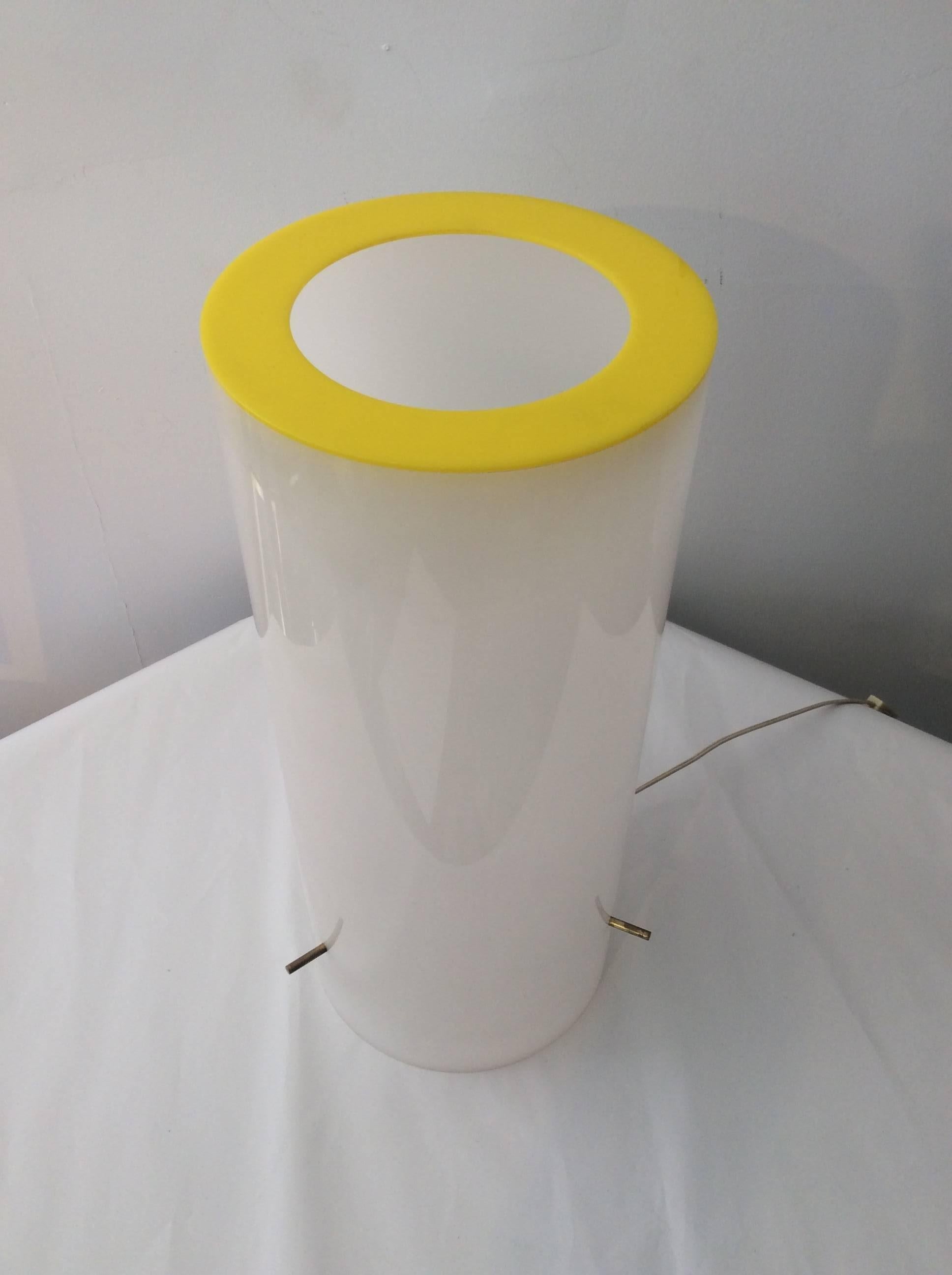 You are looking at a modern table lamp designed by Paul Mayen for Habitat. This lamp is cylindrical in shape and white in color with a yellow ring at top. The bulb mechanism is held by three brass prongs. It uses a regular type bulb. The wiring is