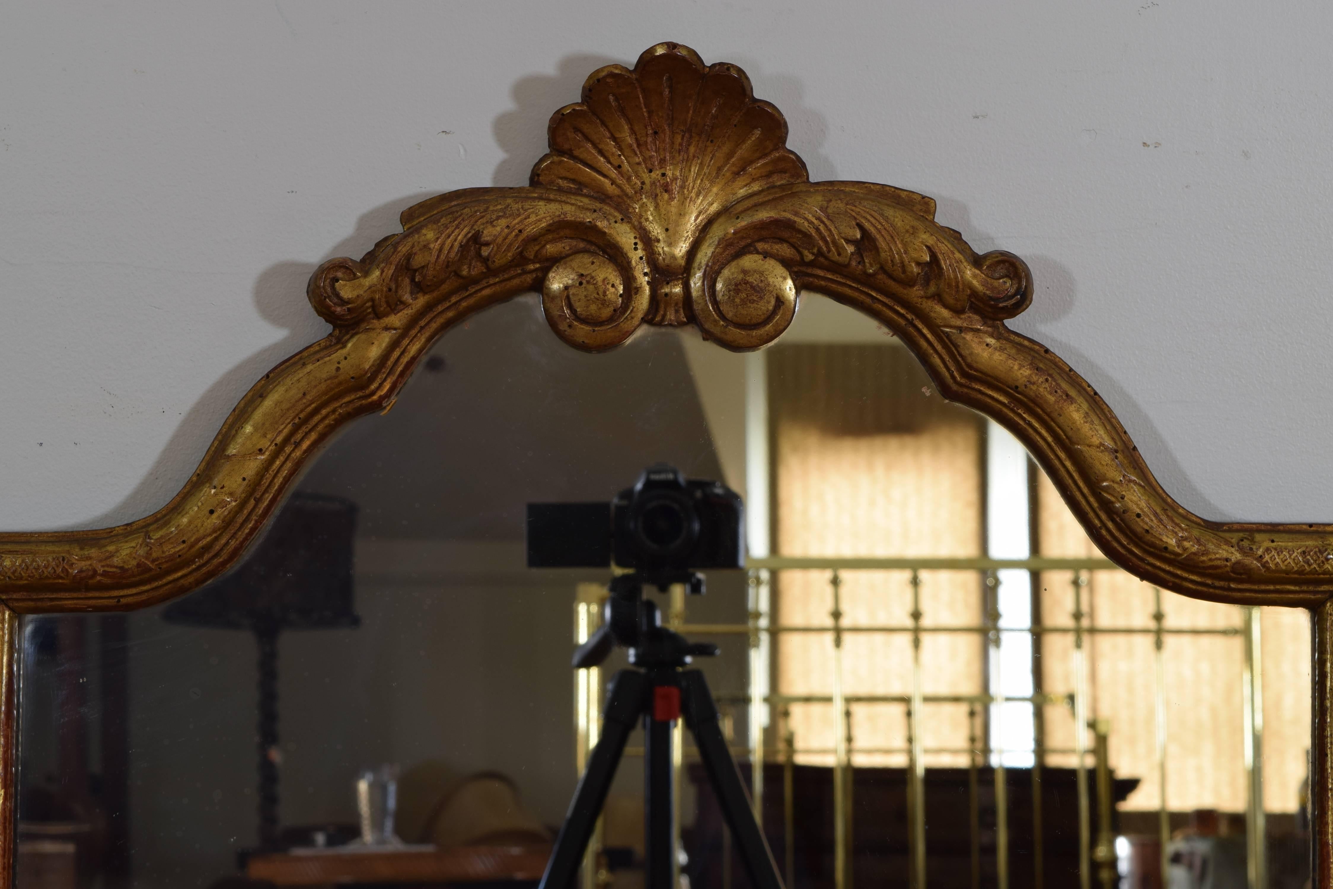 The rectangular frame with an arched top surmounted by a shell carving atop foliage carved scrolls, the entire frame adorned throughout with decorative carvings, perfect dimensions for a powder room mirror.