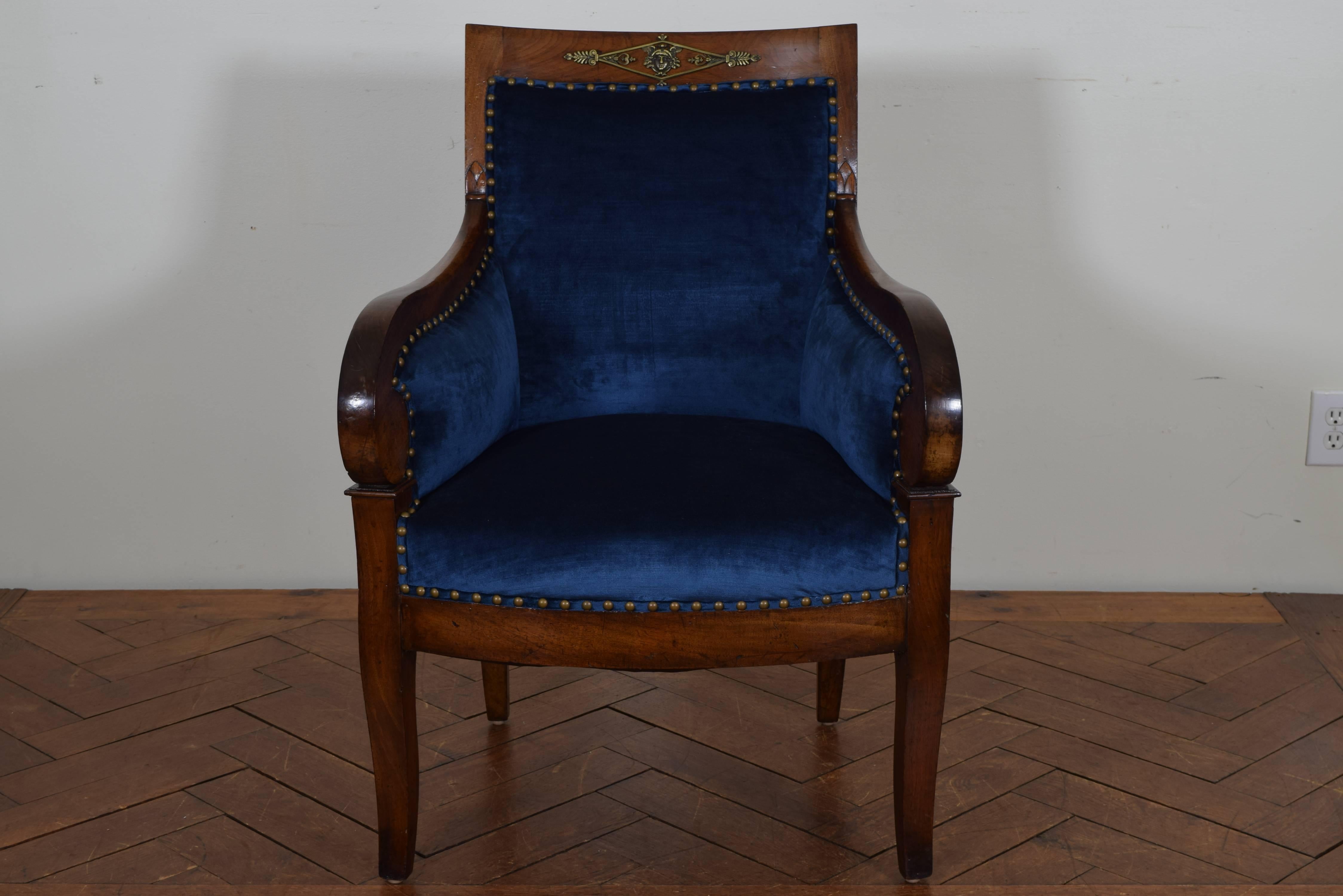 French restauration period walnut and upholstered bergere, late first quarter of the 19th century, having a curved backrest with slight carvings at sides and a bronze-mounted decorative mask of mercury at upper section, the graceful arms extending