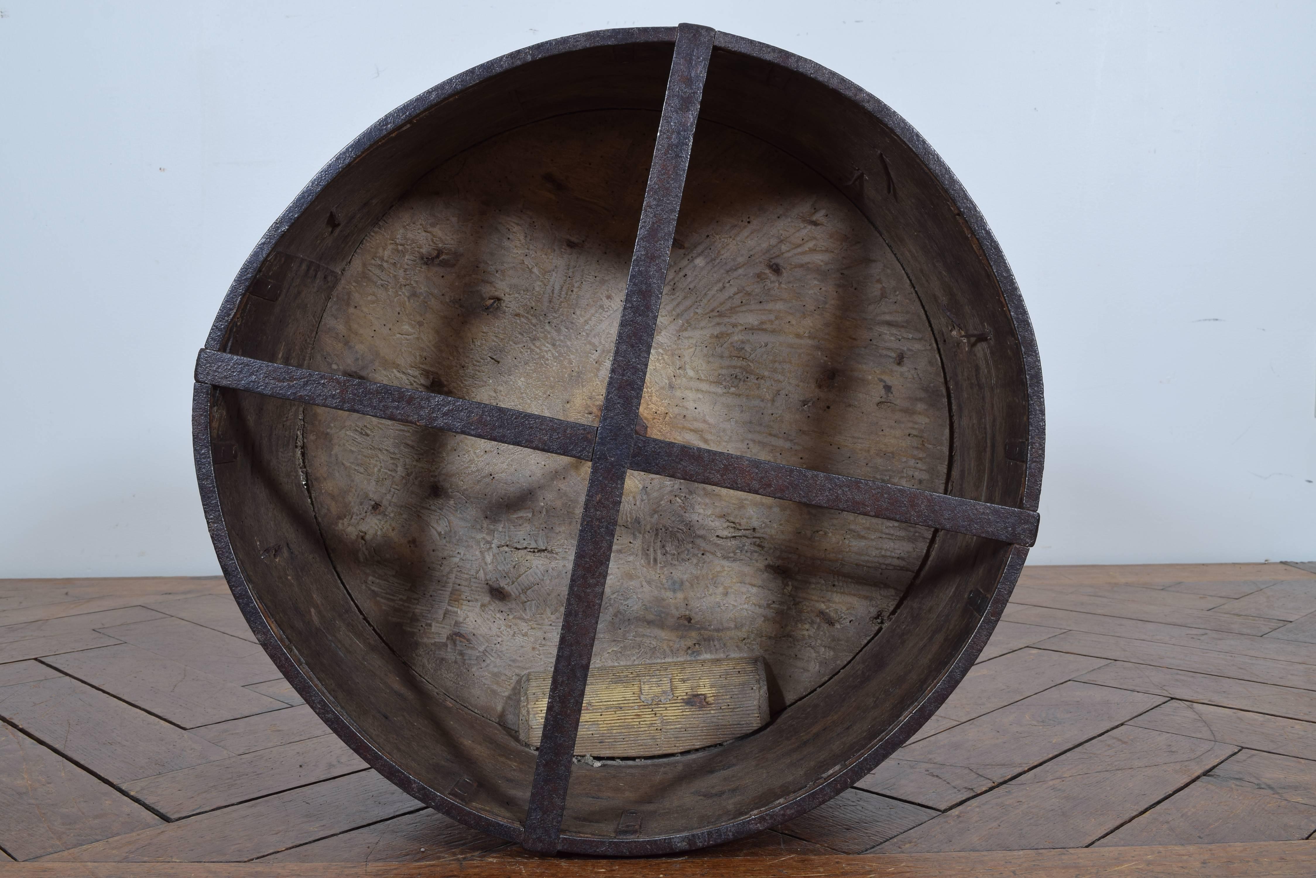 Of cylindrical form and constructed of two pieces of wood it is reinforced with iron bracing and decorated overall with iron scrolls and trefoils as well as bound by iron straps, the function was to provide an official measure of grain, the small