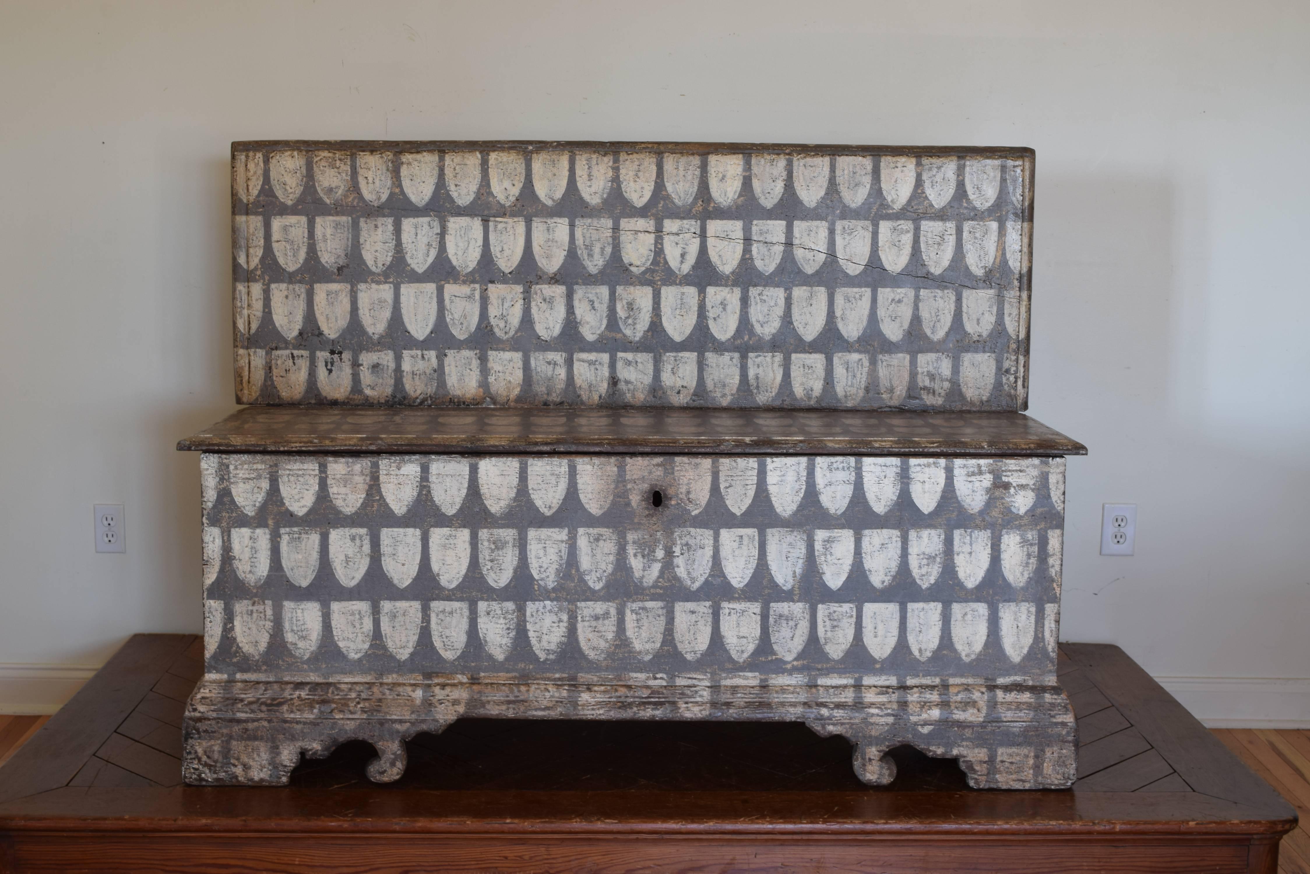 Having a straight back with the hinged top opening to reveal a storage well, raised on a plinth base and shaped bracket feet. Decorated overall with shield shapes in grey and white.