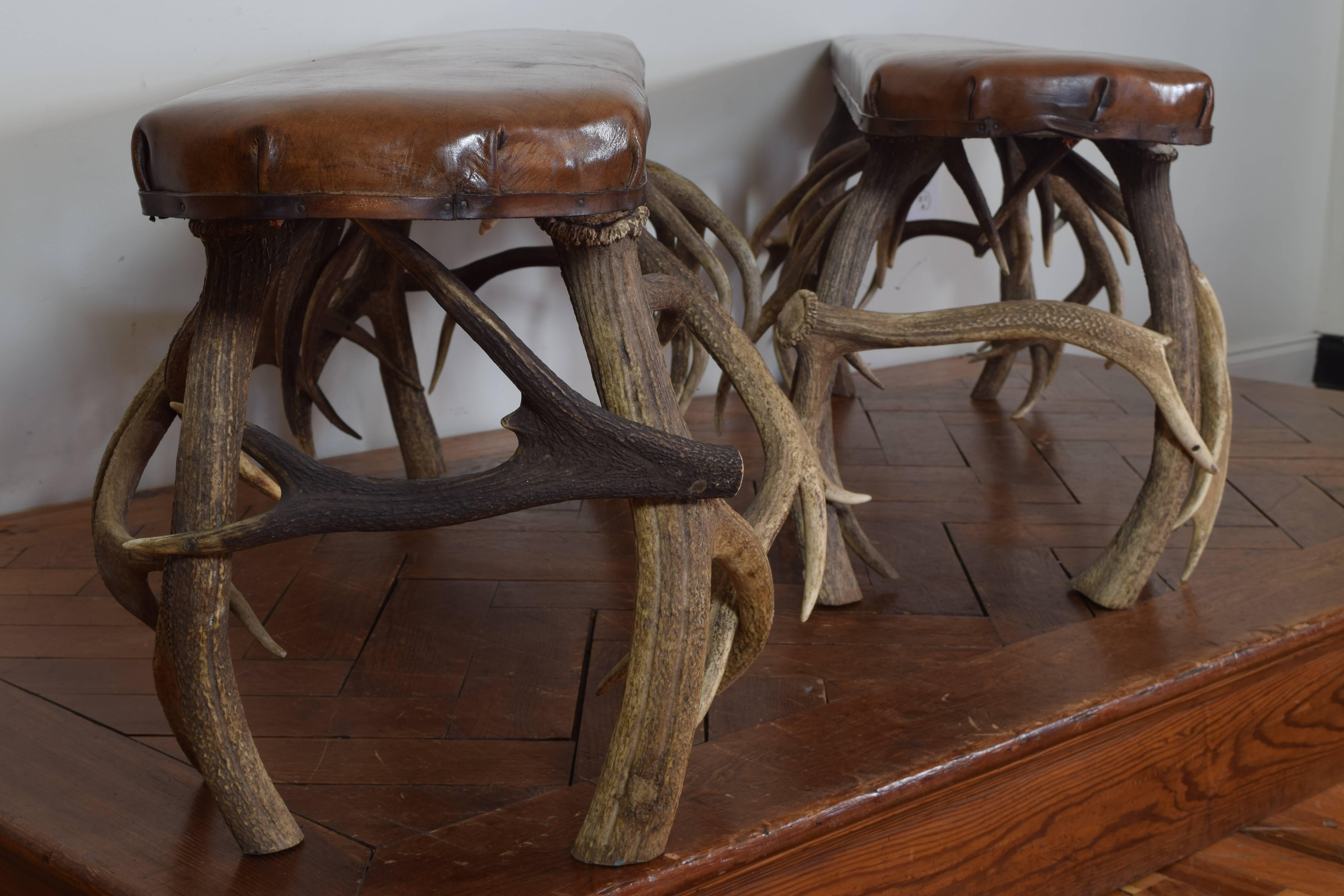 The leather upholstered rectangular tops with rounded ends and resting atop securely placed legs of antlers, first half of the 20th century.