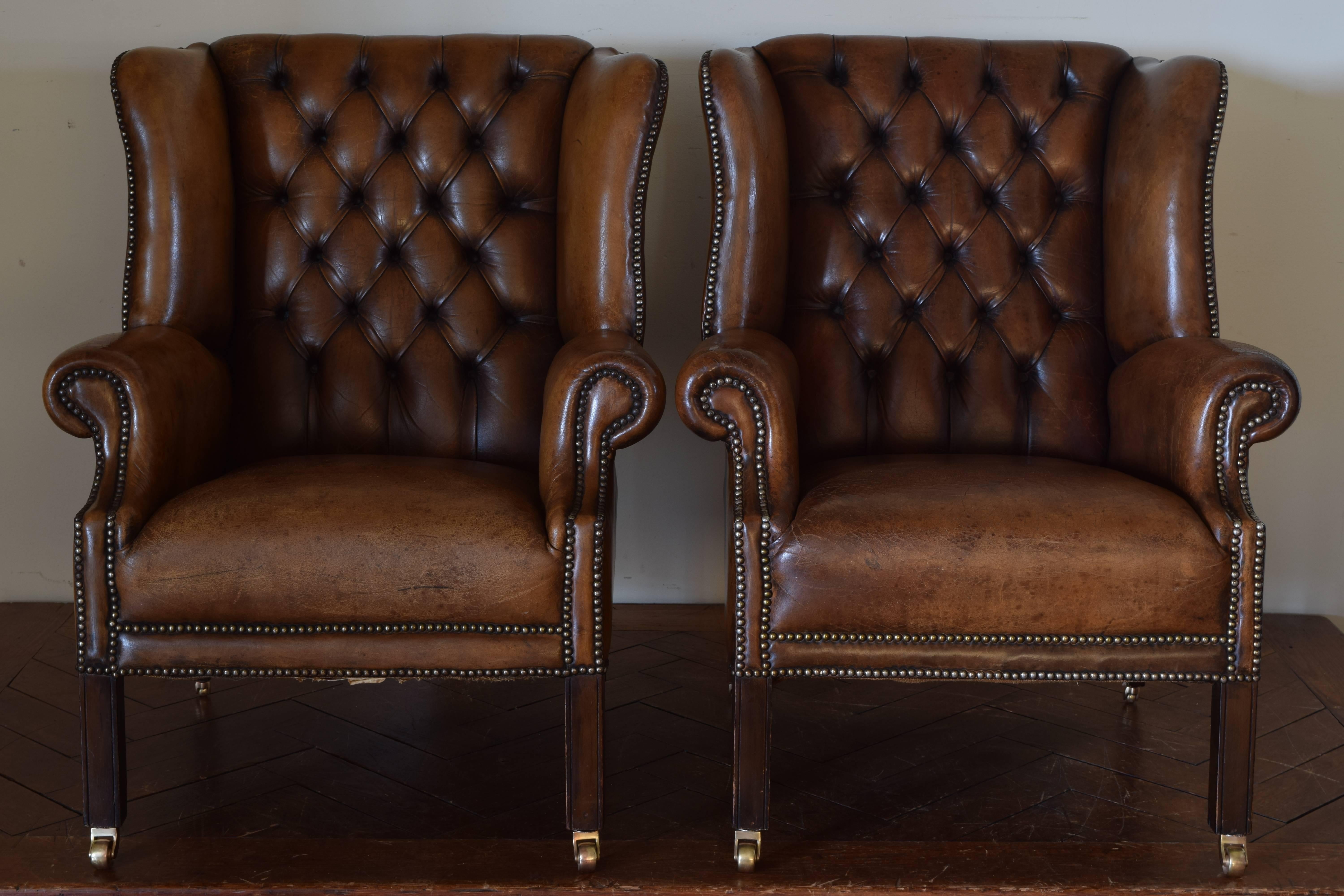 Raised on mahogany legs with brass wheels, upholstered in leather with tufted backrests.