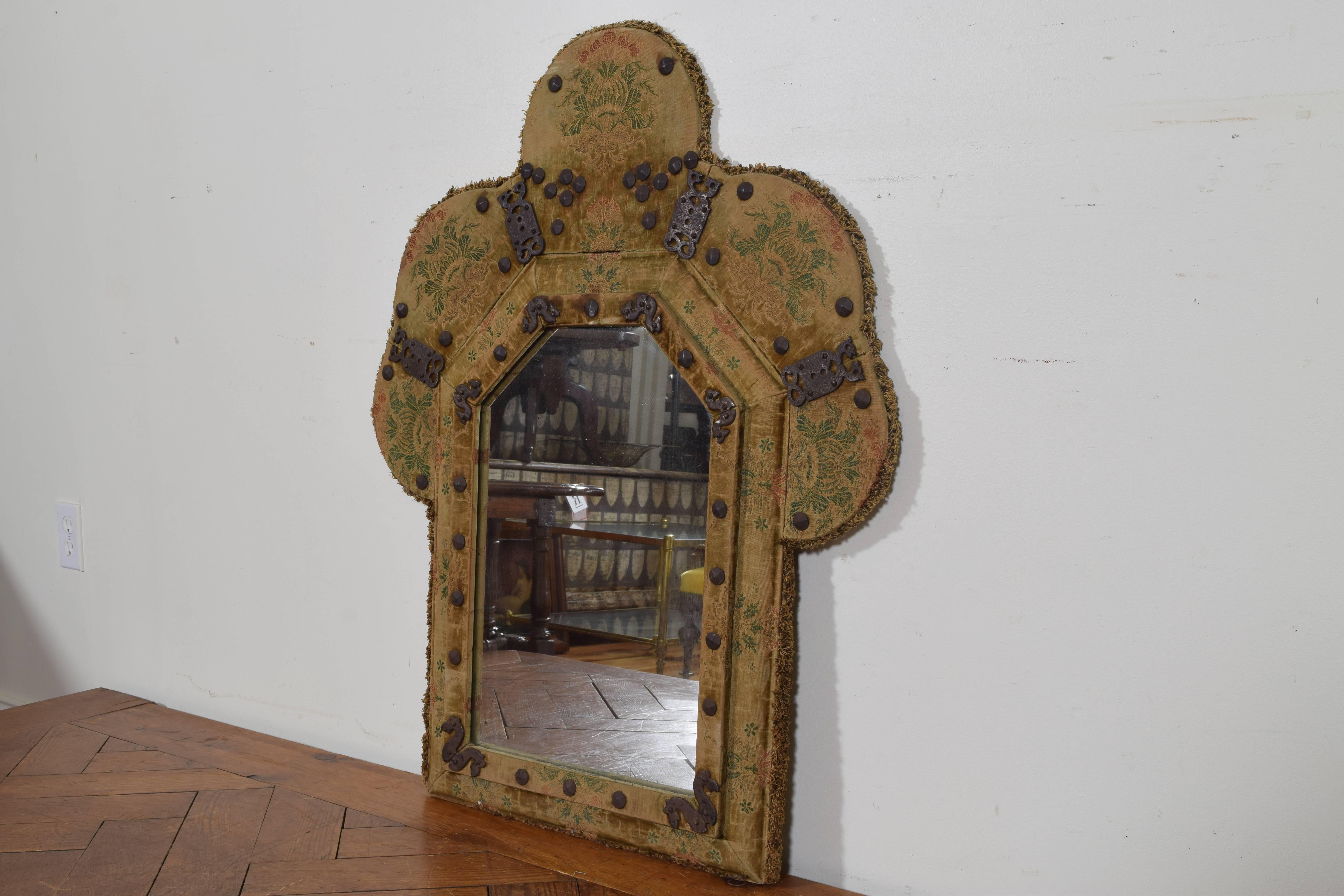 Covered in a faded patterned velvet and mounted with iron nailheads and decorative elements, retaining an antique mirror plate.