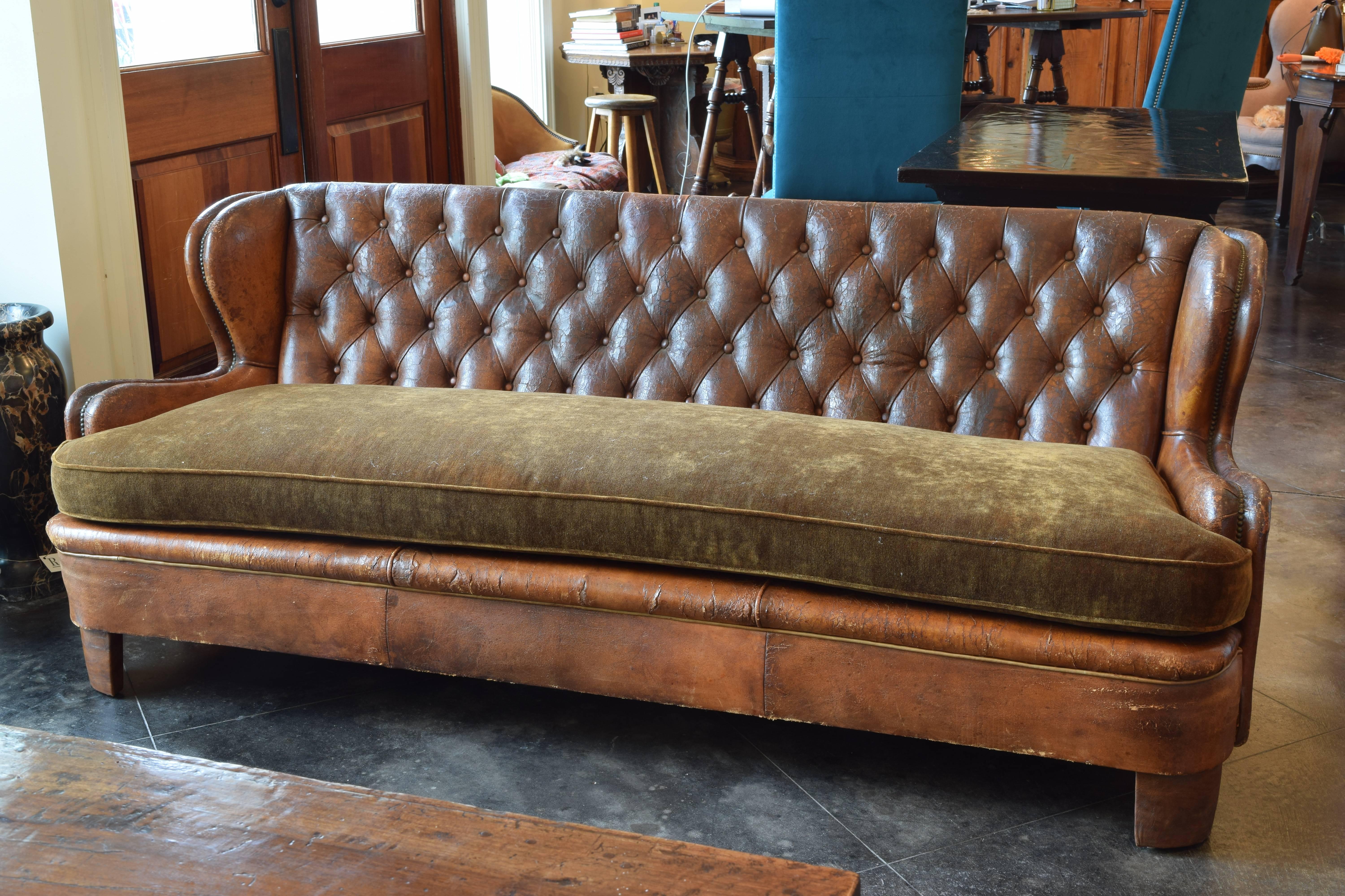 Sofa of slightly convex form with curved arms and a tufted backrest, the arms and back with a brass nailhead lined channel, with a new velvet upholstered down cushion, the feet are covered in leather, second quarter of the 20th century.