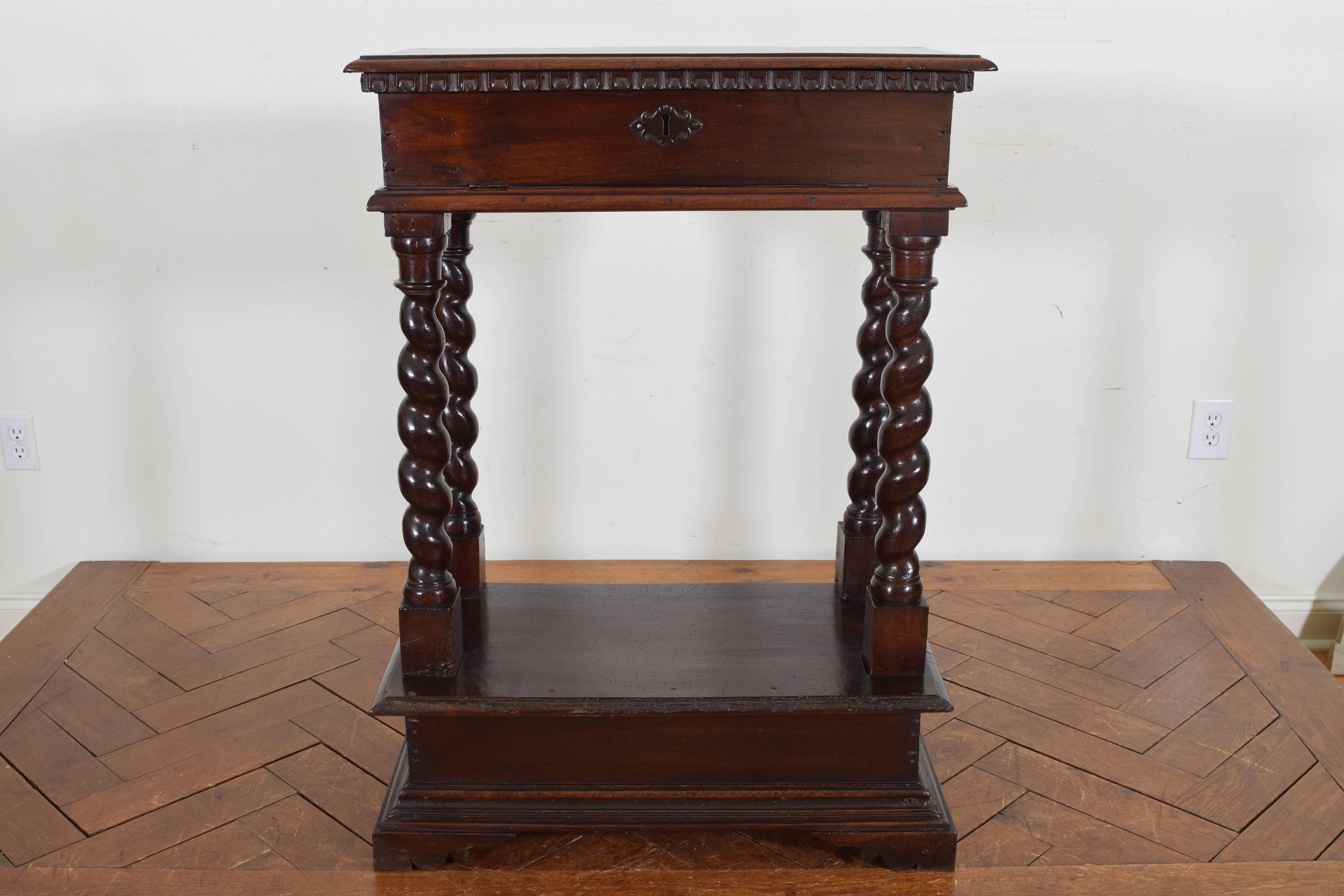 The rectangular top with dentile molding above a conforming case with flip down front revealing a storage area, raised on spiral carved supports with block feet, the whole raised on a plinth-form base.