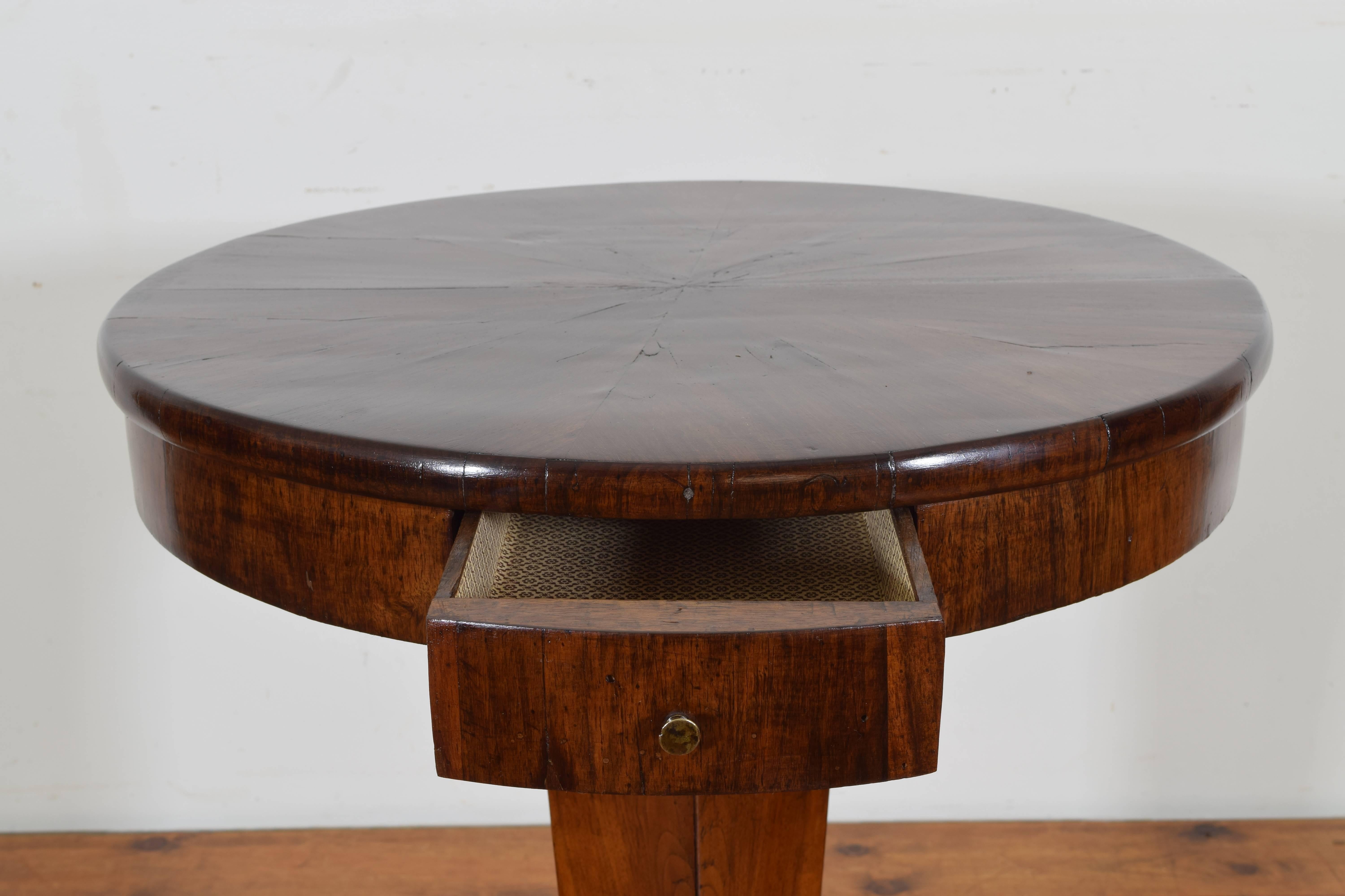 From the second quarter of the 19th century, the table covered in mahogany veneers, the round top housing one-drawer and raised on a tapering hexagonal pedestal atop a tripartite base raised on flattened feet.