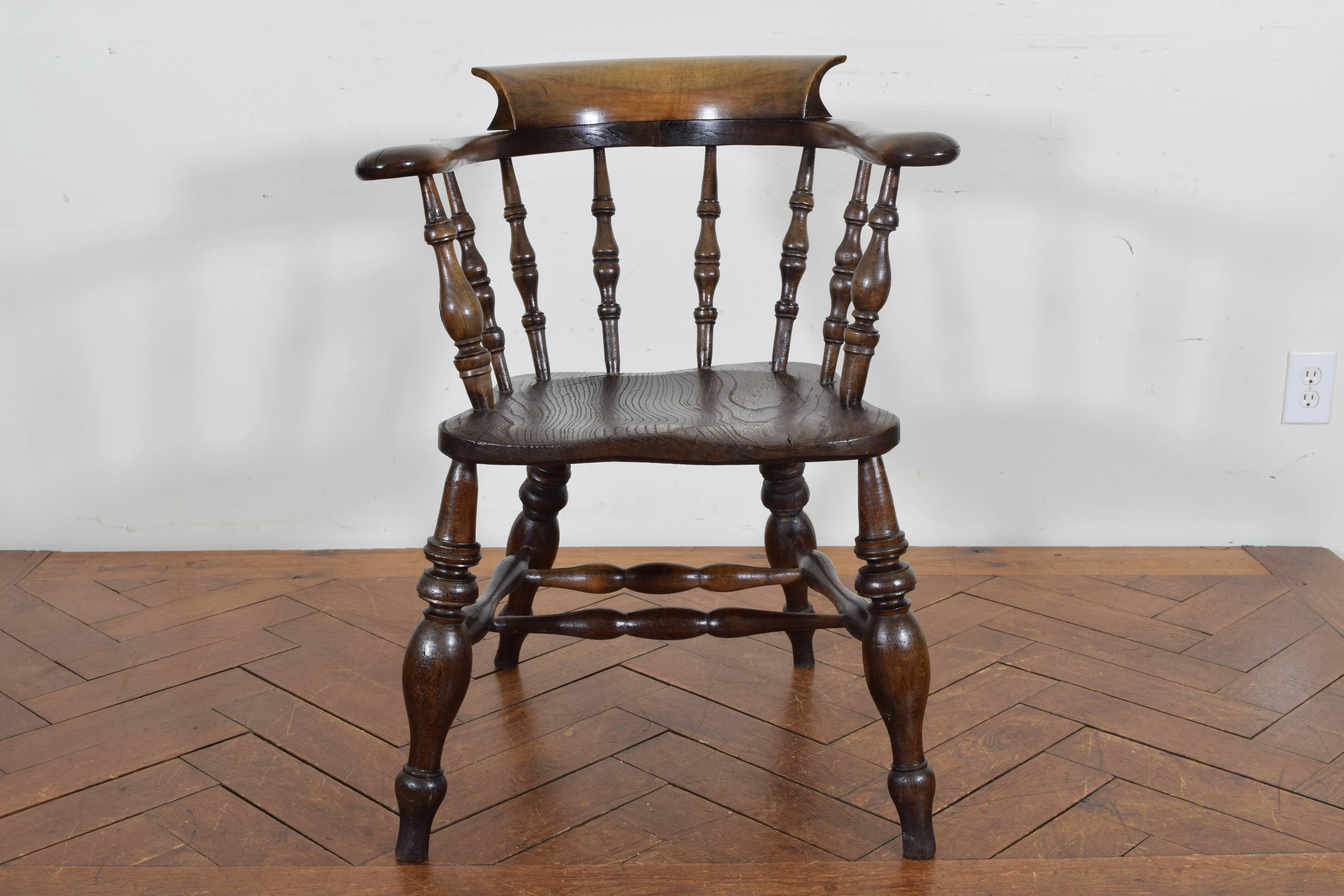 Having a curved back and upper backrest, the arms supported by turned spindles, the shaped seat above splayed turned legs joined by two stretchers.