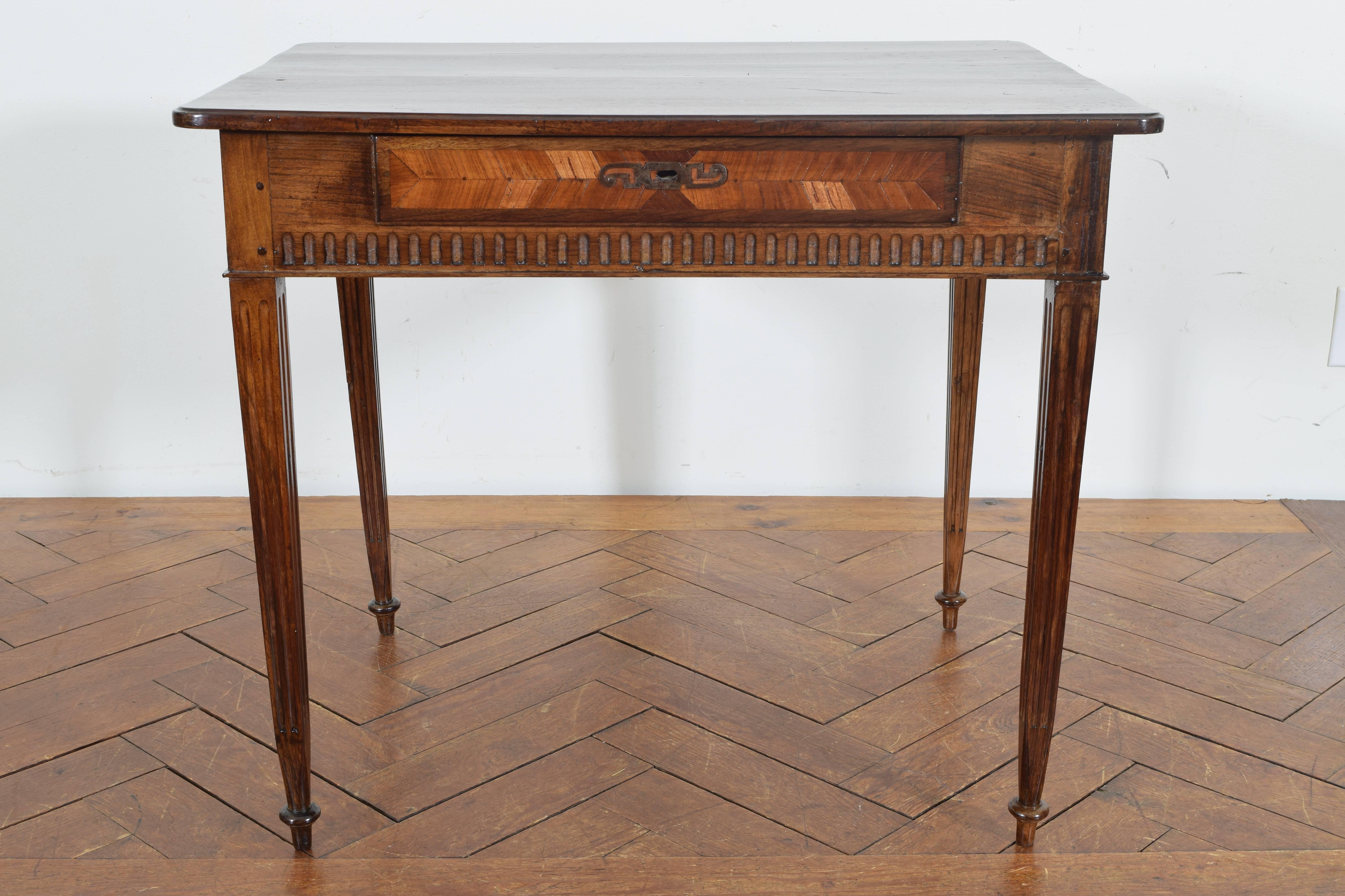 The rectangular top with rounded corners, the conforming case with detail carvings and housing one veneered drawer, raised on fluted tapering legs ending in turned feet.