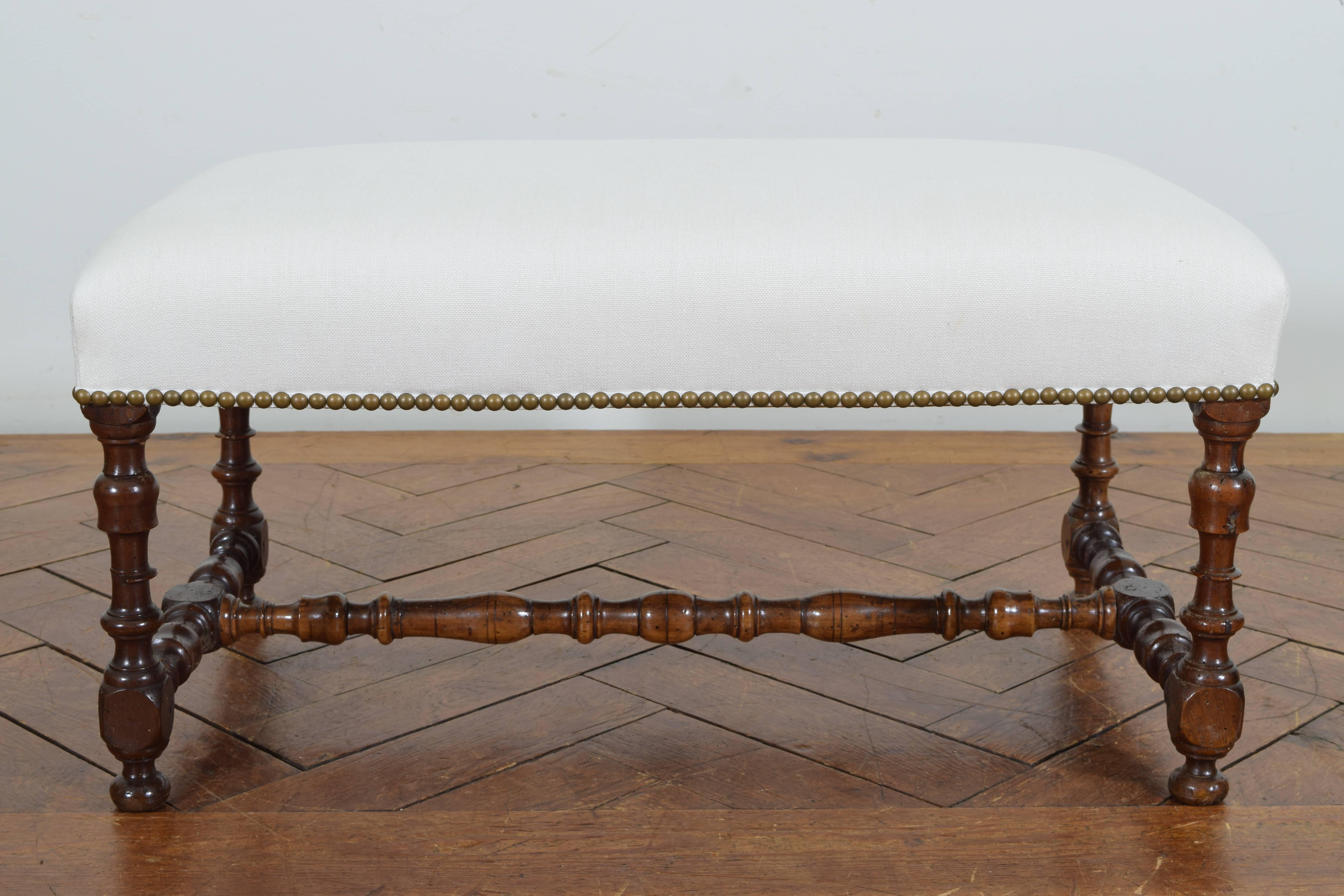 The rectangular top upholstered in white linen with nailhead trim, raised on turned legs with flattened ball feet, connected by an h-form stretcher.