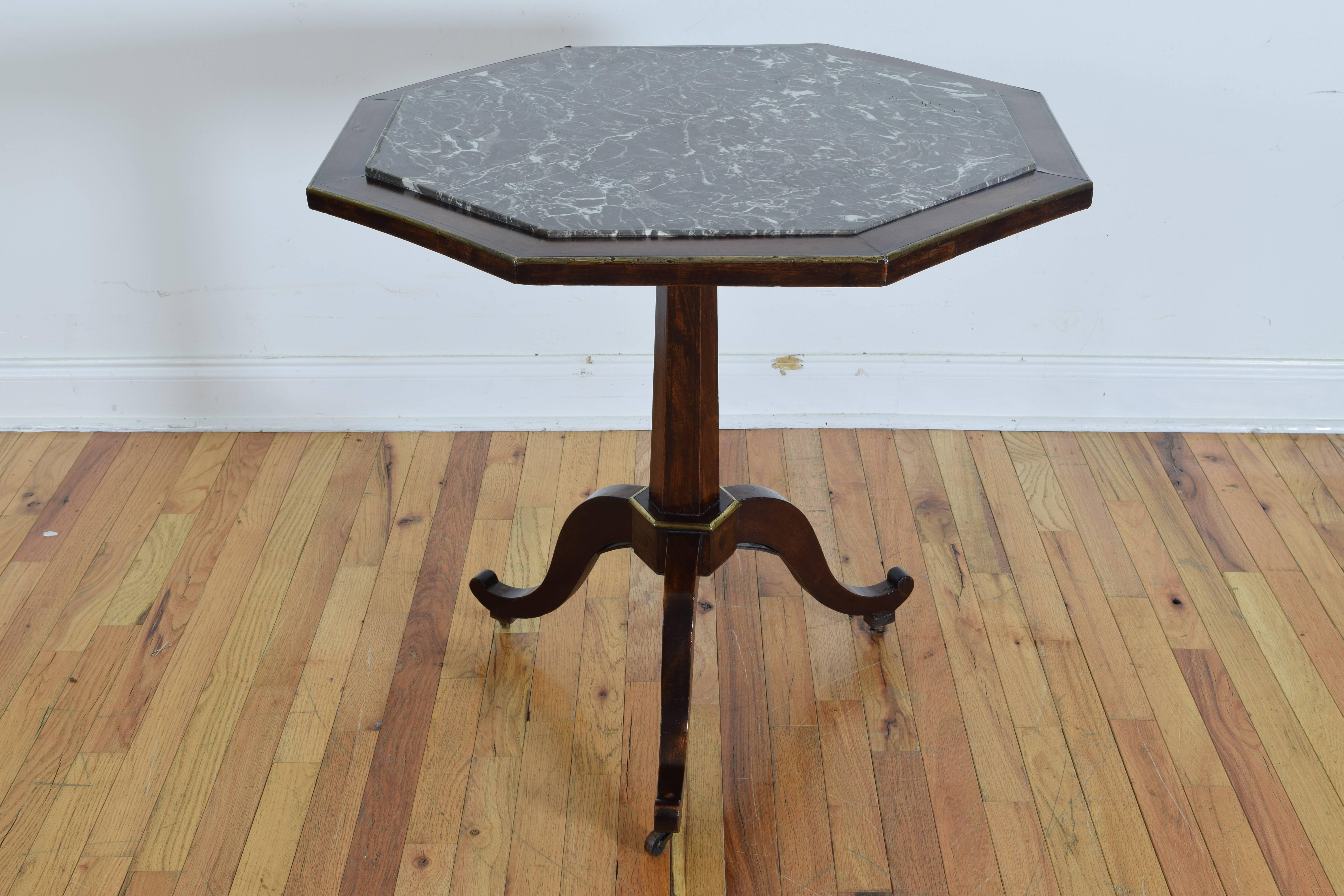 The octagonal top with a large inset marble center, trimmed in brass, the hexagonal columnar support terminating at a tripartite base issuing three scrolling legs with upturned feet and original wooden casters.